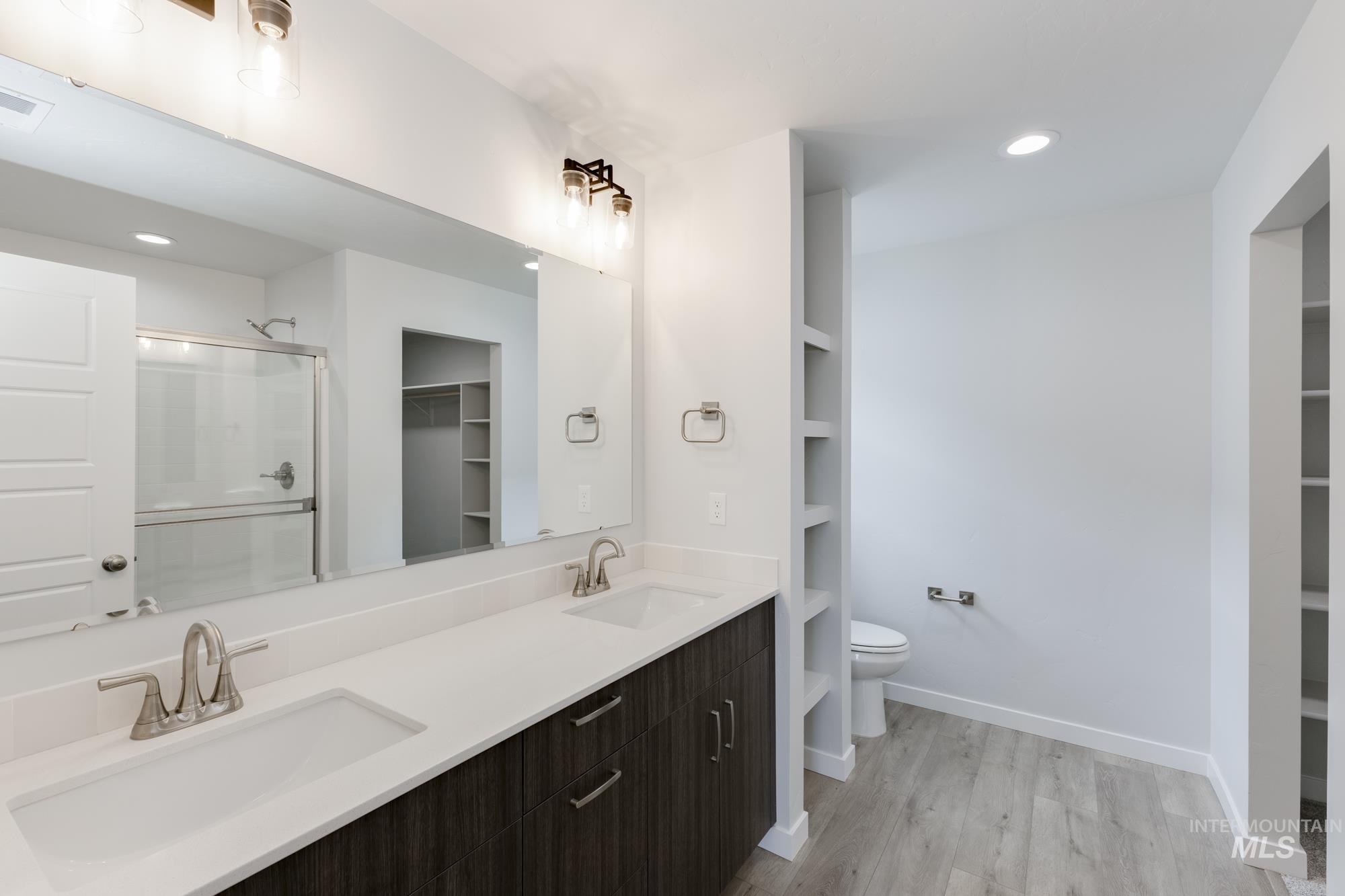 Bathroom featuring a spacious closet, a shower stall, light wood-style flooring, recessed lighting, and double vanity