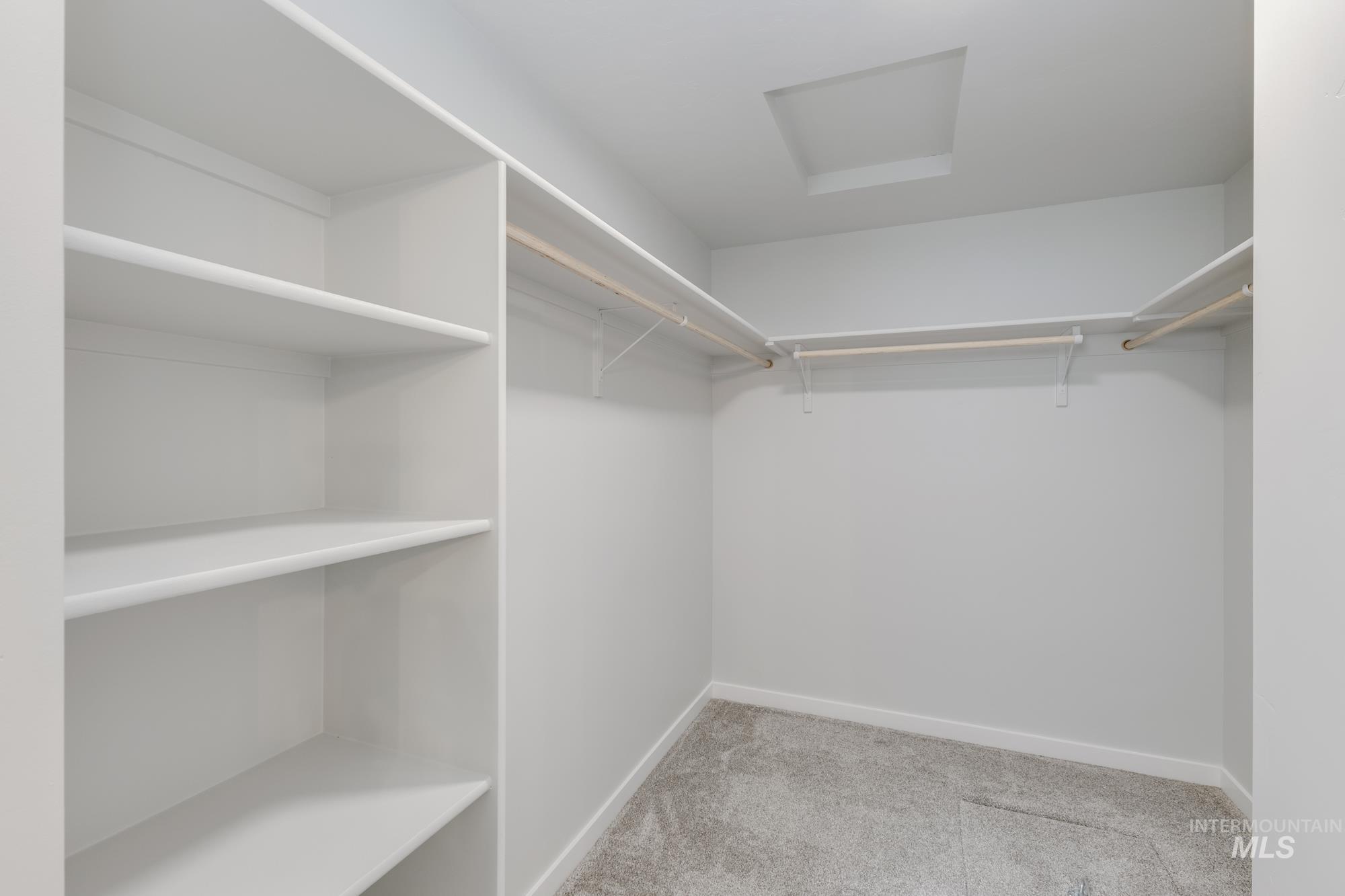Walk in closet with light colored carpet and attic access
