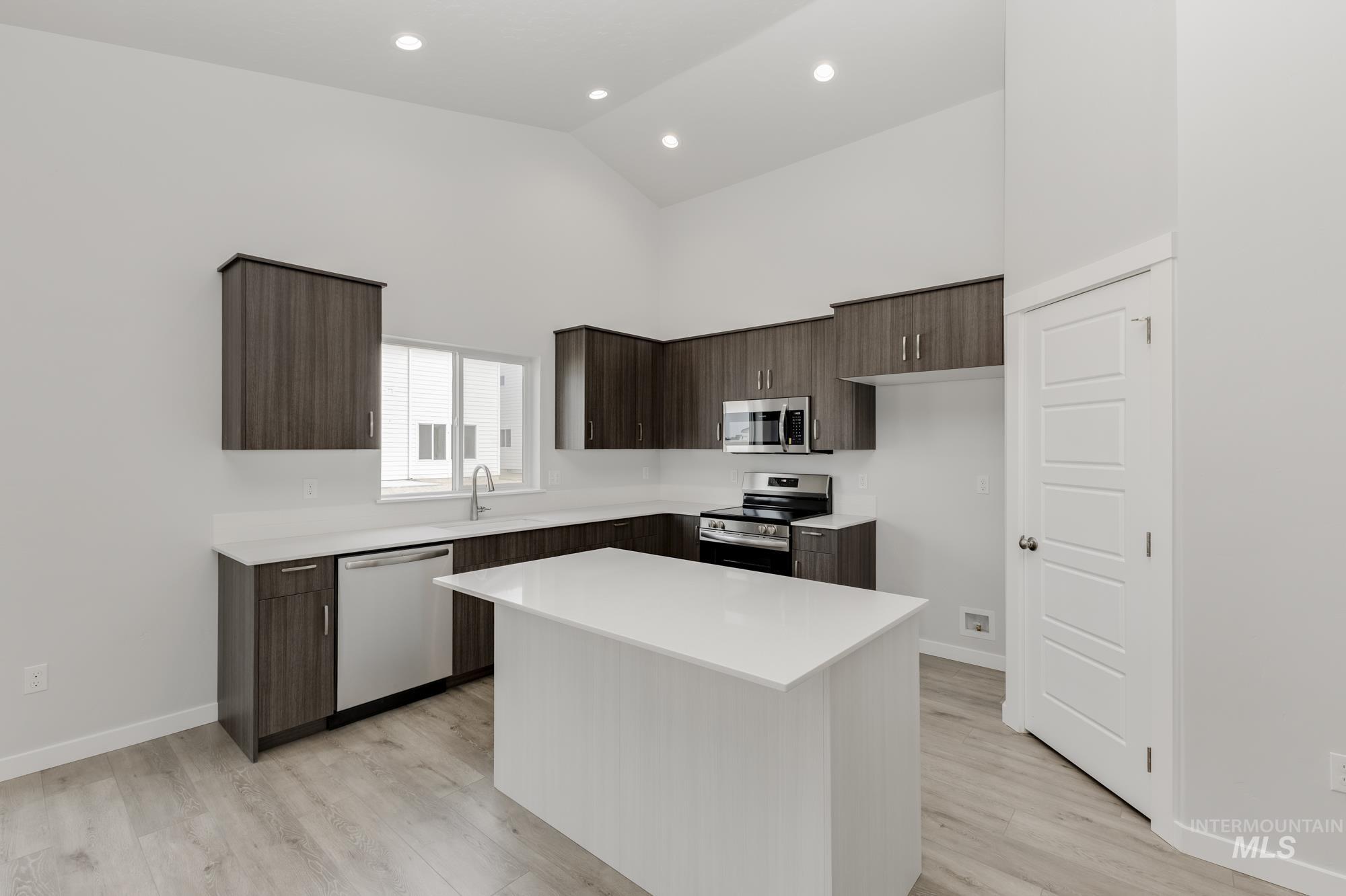 Kitchen featuring dark brown cabinets, appliances with stainless steel finishes, high vaulted ceiling, modern cabinets, and a kitchen island