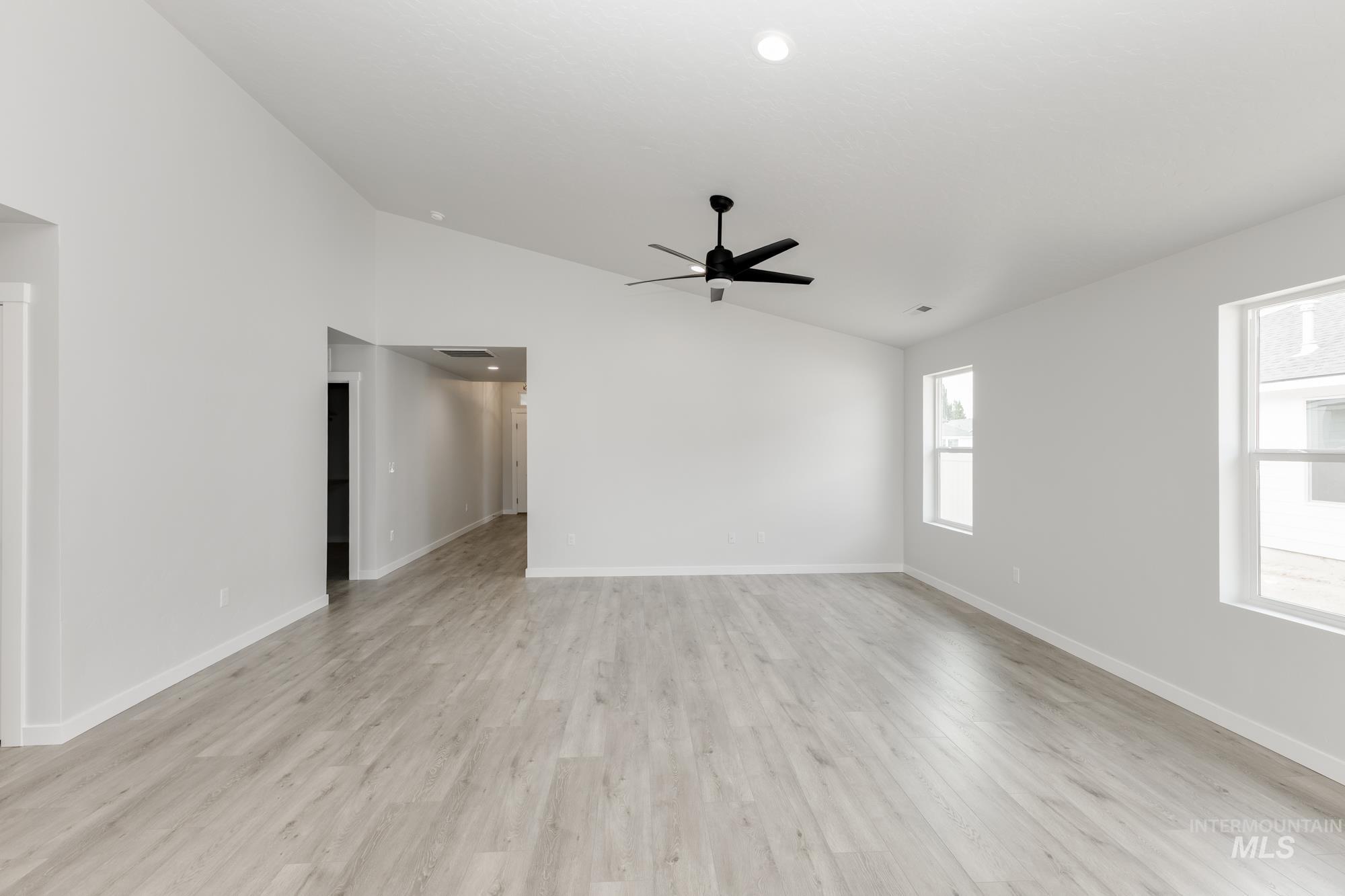 Empty room with vaulted ceiling, light wood finished floors, and a ceiling fan