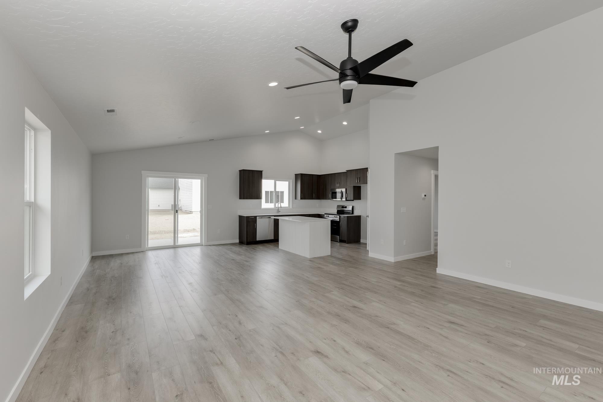 Unfurnished living room with light wood-type flooring, a ceiling fan, a textured ceiling, and high vaulted ceiling