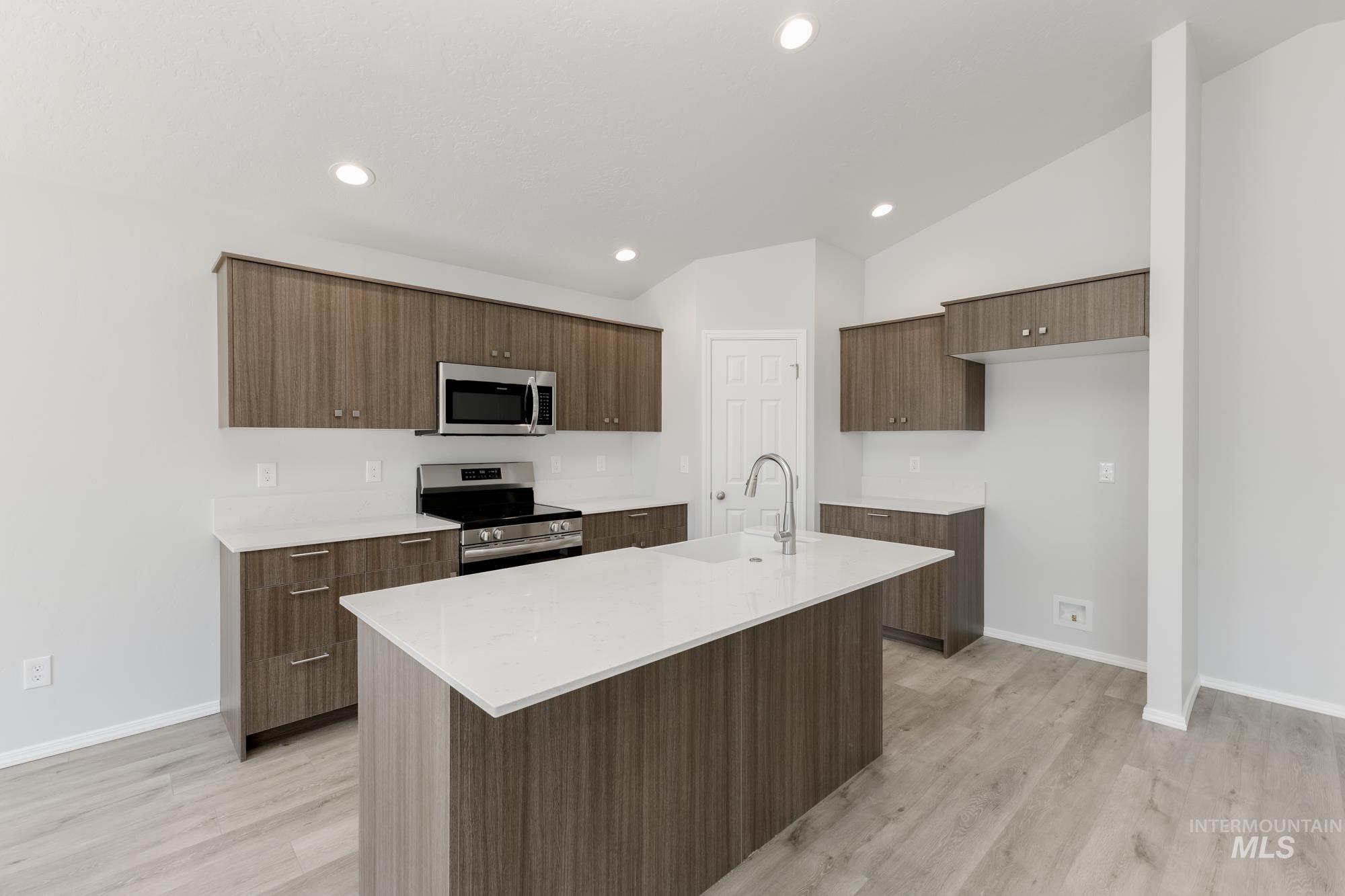 Kitchen featuring vaulted ceiling, stainless steel appliances, light countertops, modern cabinets, and an island with sink