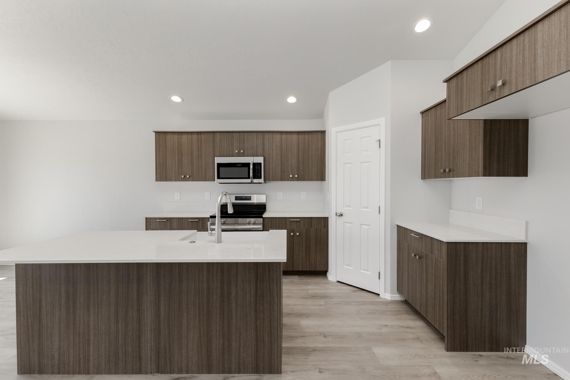 Kitchen featuring appliances with stainless steel finishes, light wood-style floors, light countertops, an island with sink, and recessed lighting