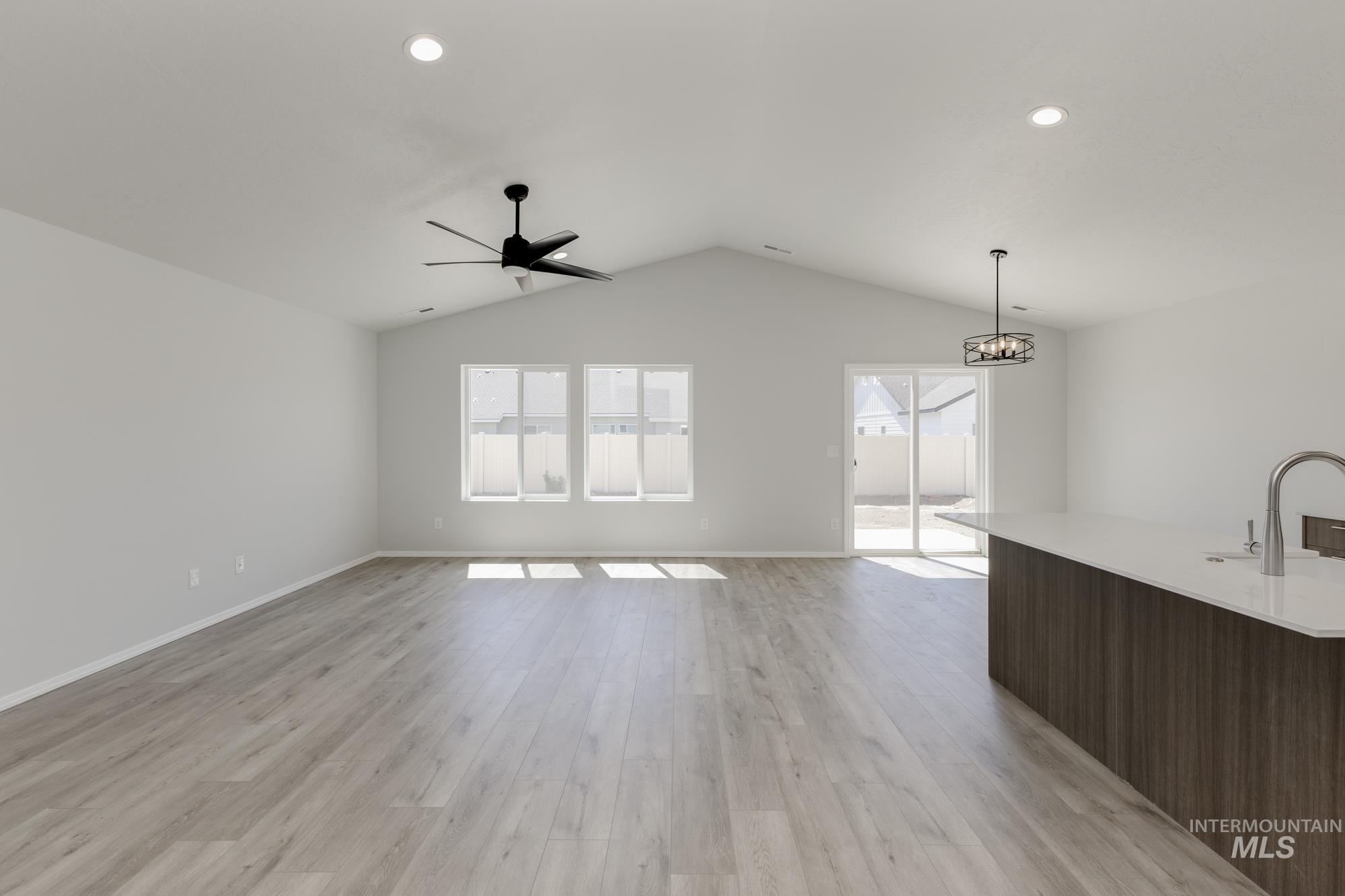 Unfurnished living room featuring light wood-style floors, ceiling fan, recessed lighting, a chandelier, and vaulted ceiling