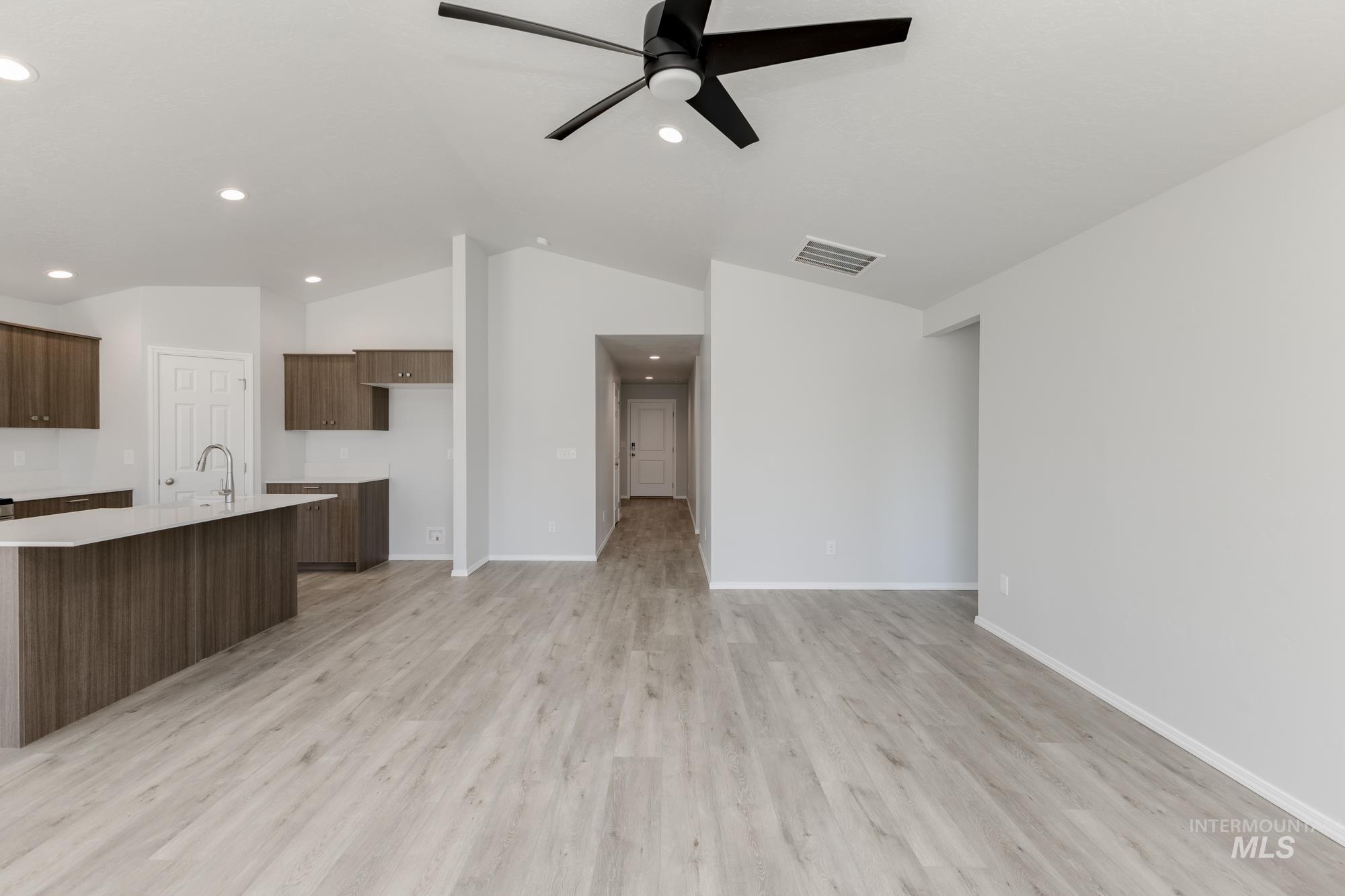 Kitchen with vaulted ceiling, light countertops, a ceiling fan, light wood finished floors, and a center island with sink