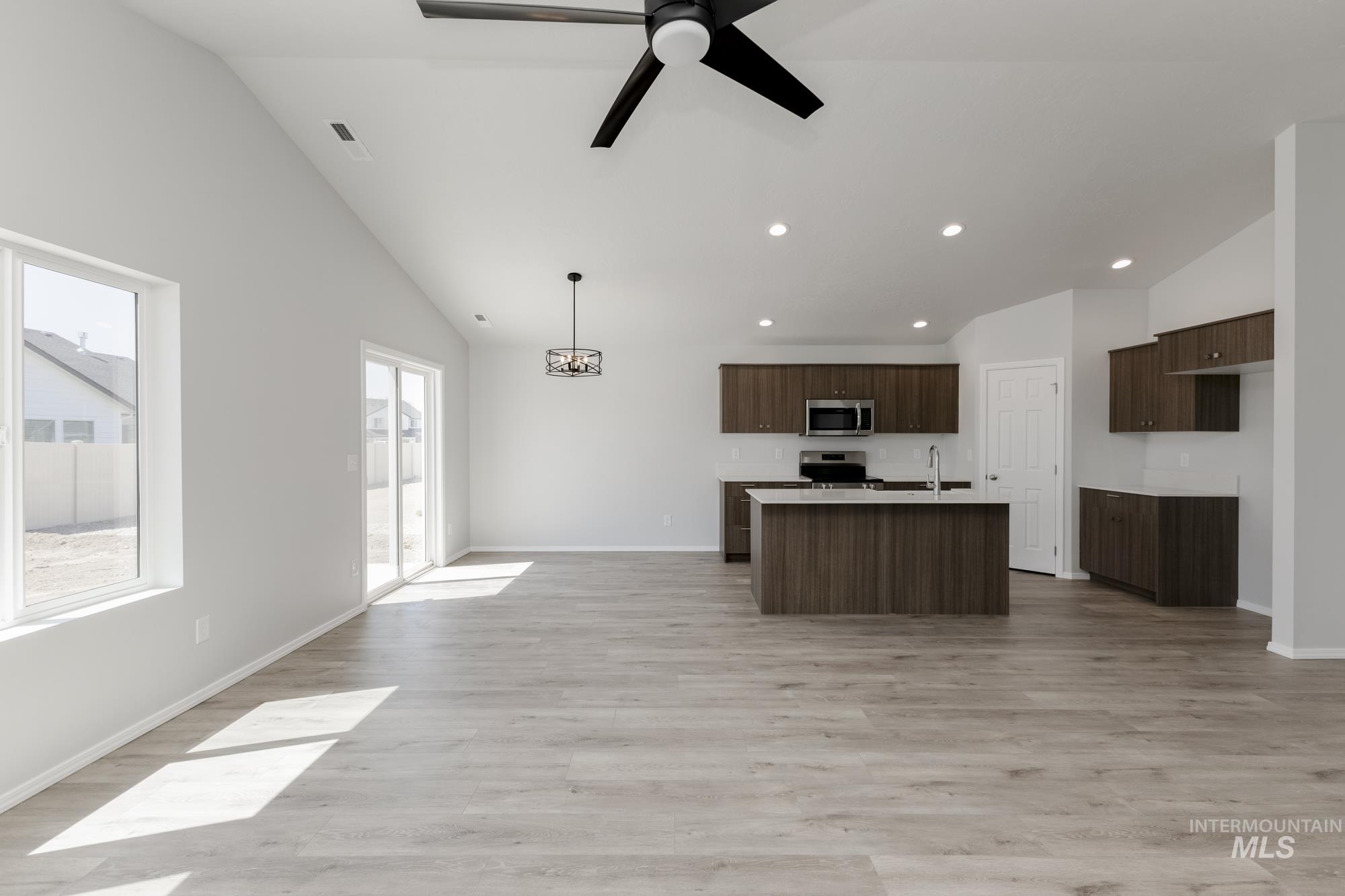 Kitchen featuring open floor plan, light wood-style flooring, an island with sink, high vaulted ceiling, and a ceiling fan