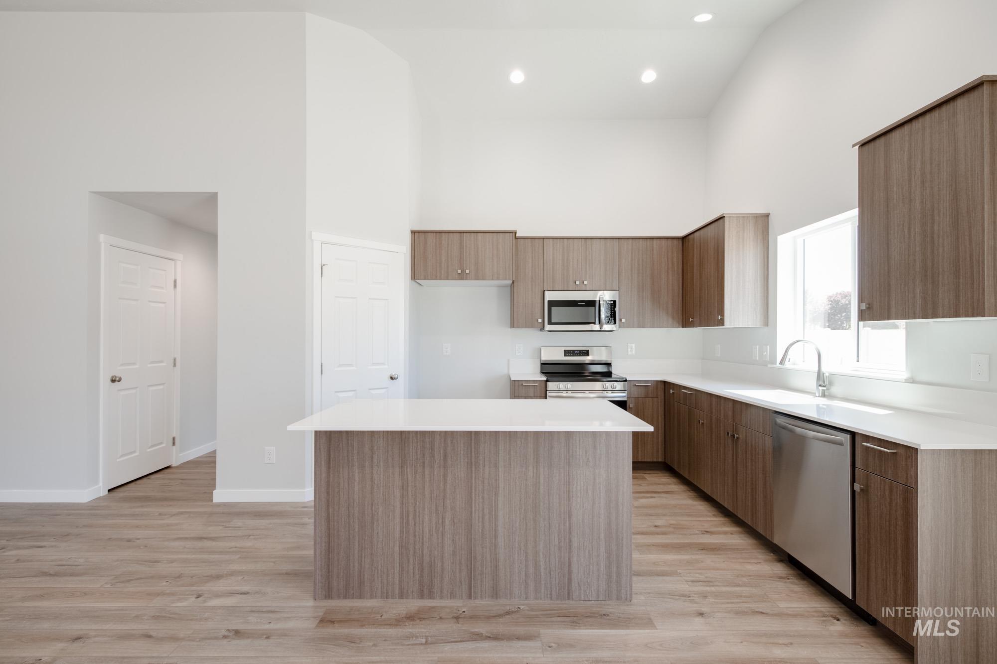 Kitchen with light wood-style floors, a center island, stainless steel appliances, light countertops, and a towering ceiling