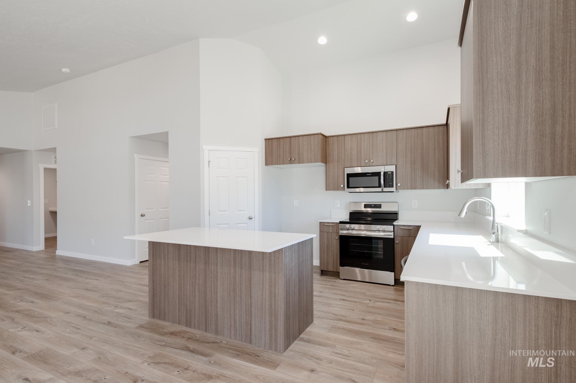 Kitchen with appliances with stainless steel finishes, light wood-style flooring, light countertops, a center island, and a high ceiling