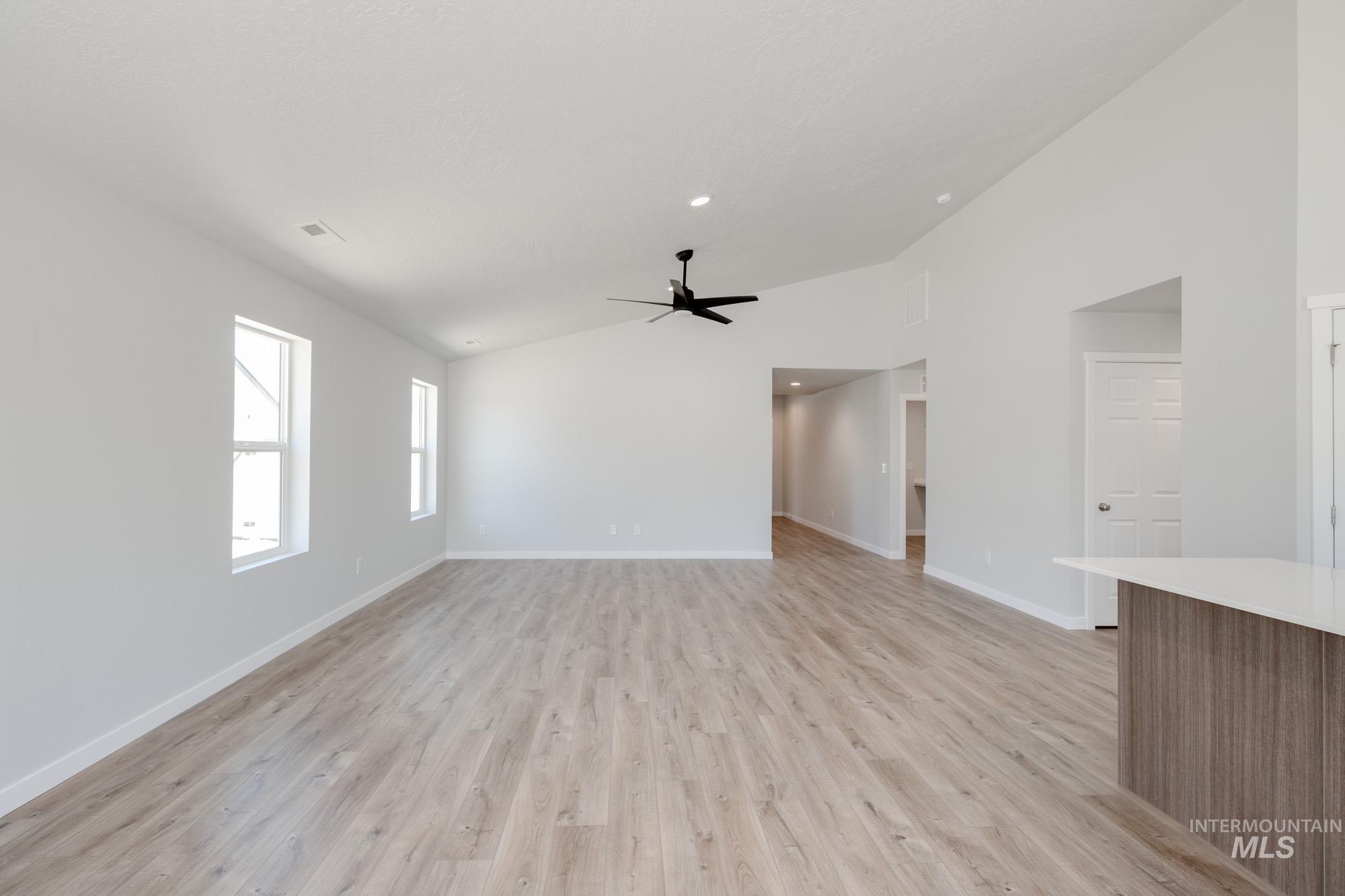 Unfurnished living room featuring lofted ceiling, light wood-type flooring, and ceiling fan