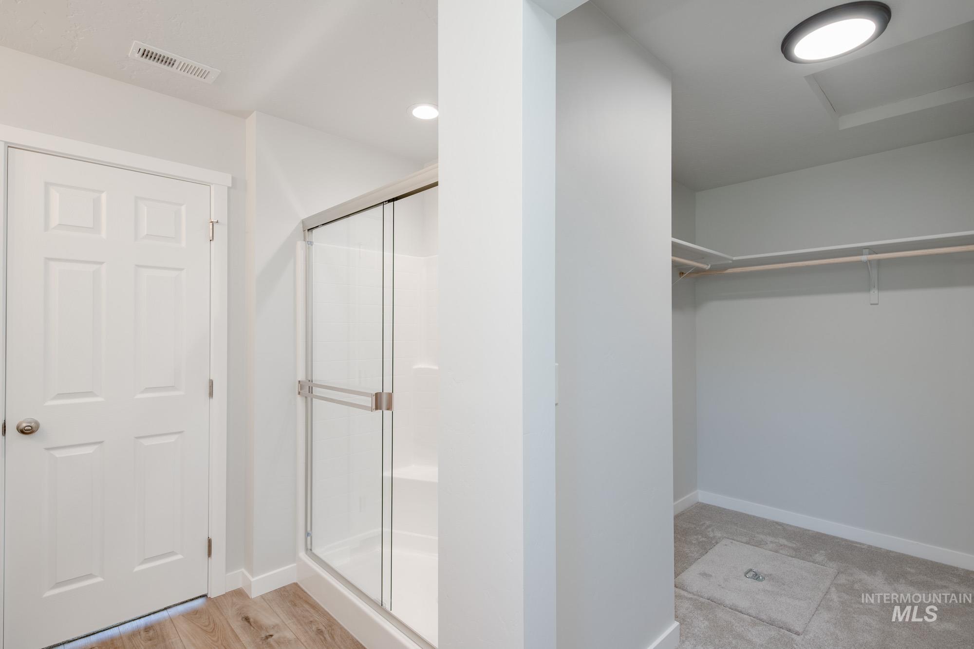 Full bathroom featuring a stall shower, a walk in closet, and wood finished floors