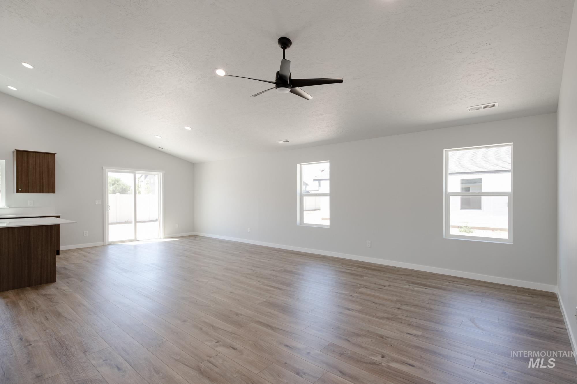 Unfurnished living room featuring wood finished floors, vaulted ceiling, a ceiling fan, and recessed lighting