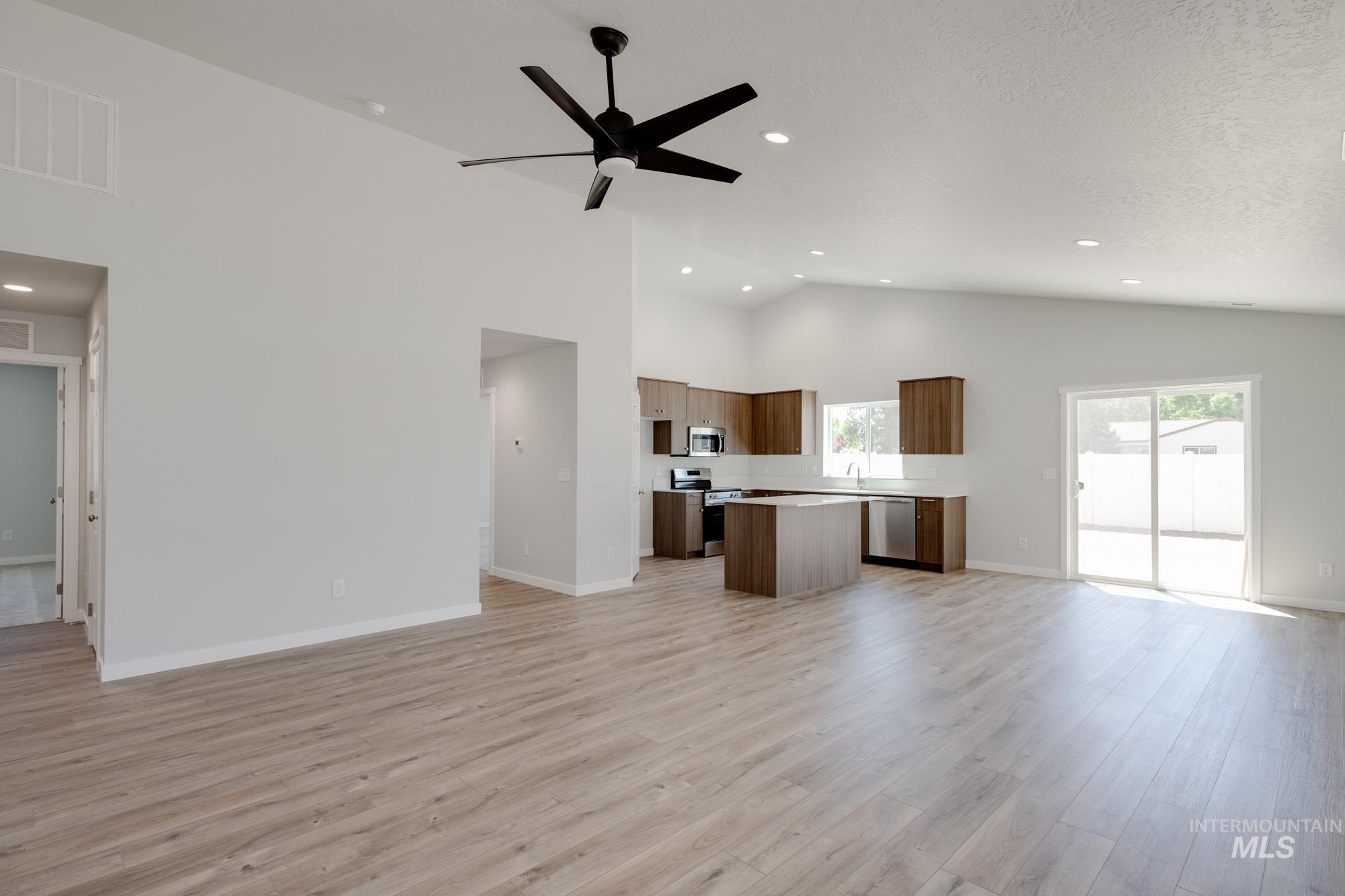Unfurnished living room with light wood-style floors, ceiling fan, high vaulted ceiling, recessed lighting, and a textured ceiling