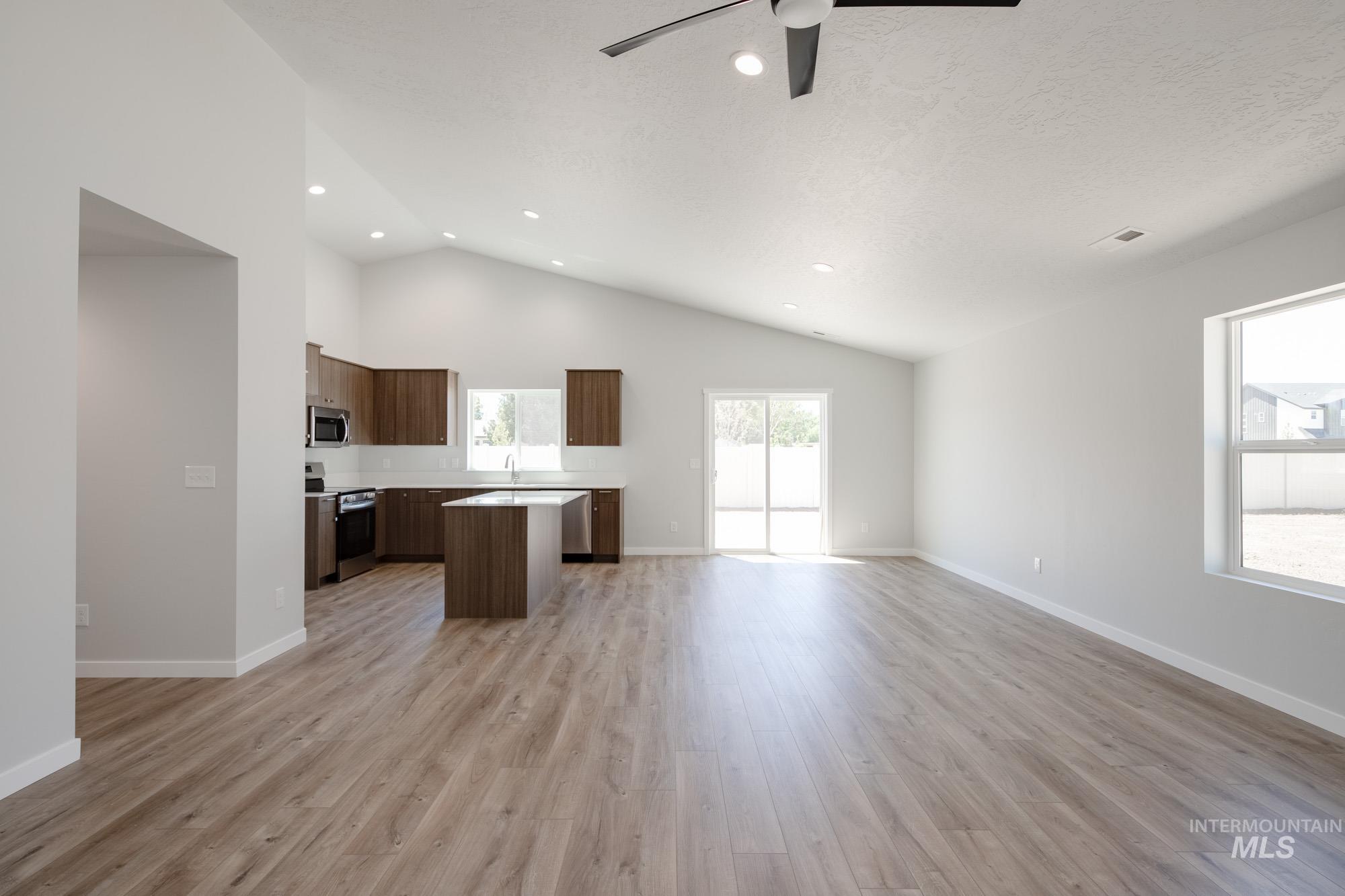 Kitchen featuring open floor plan, a kitchen island, light countertops, appliances with stainless steel finishes, and light wood-style floors