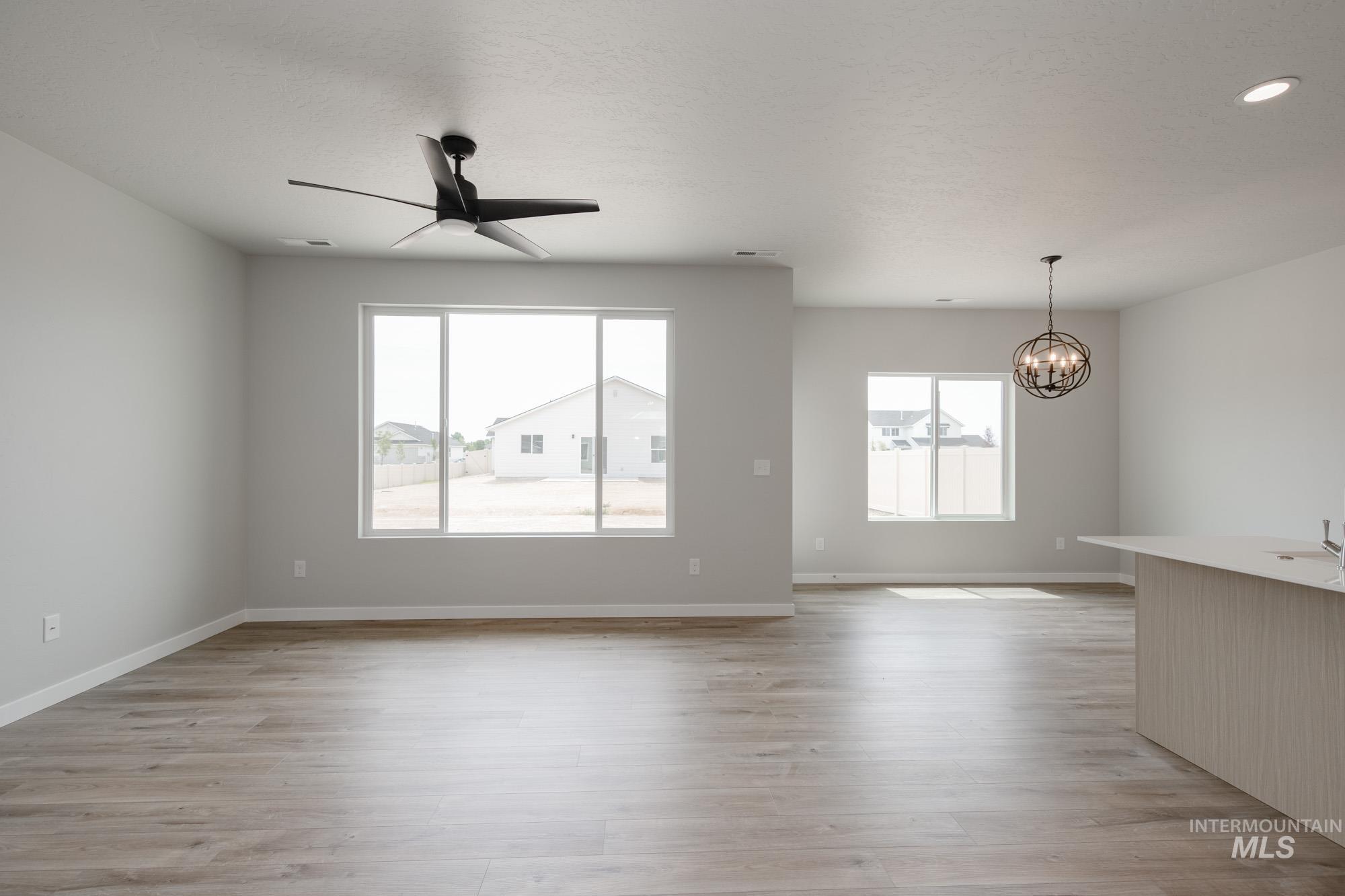 Unfurnished living room with light wood finished floors, a ceiling fan, a chandelier, and a textured ceiling