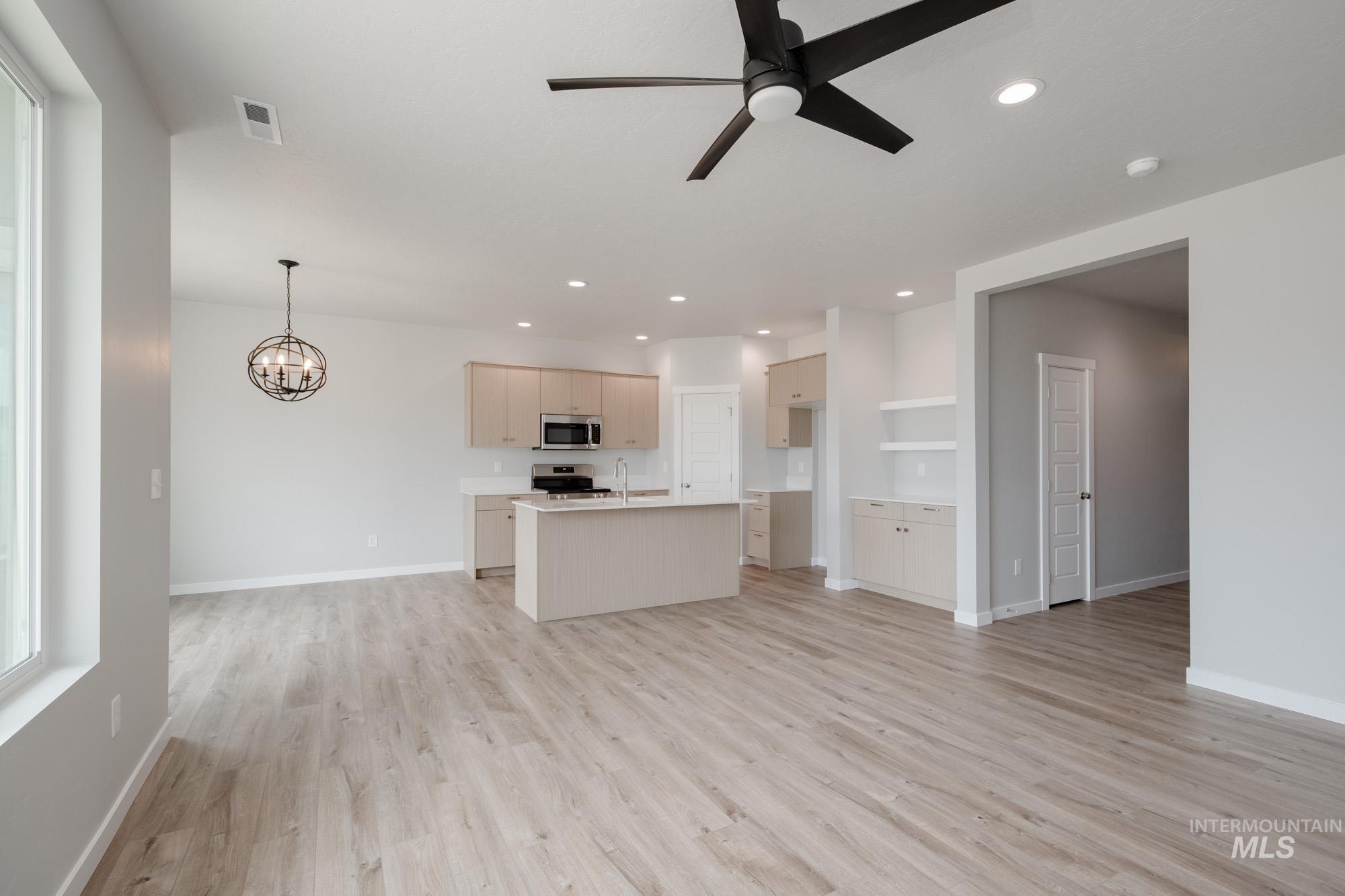 Unfurnished living room with ceiling fan, light wood-style floors, recessed lighting, and a chandelier