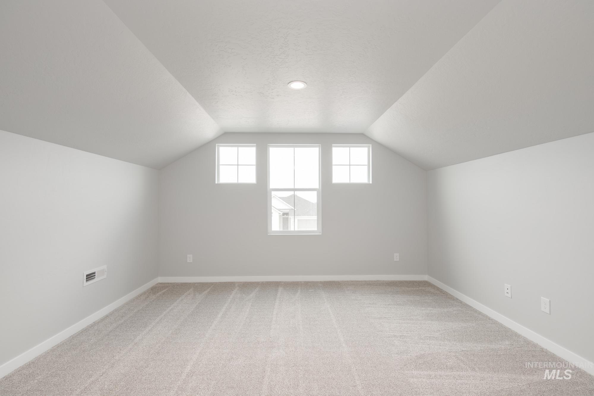Bonus room featuring light colored carpet, lofted ceiling, and a textured ceiling