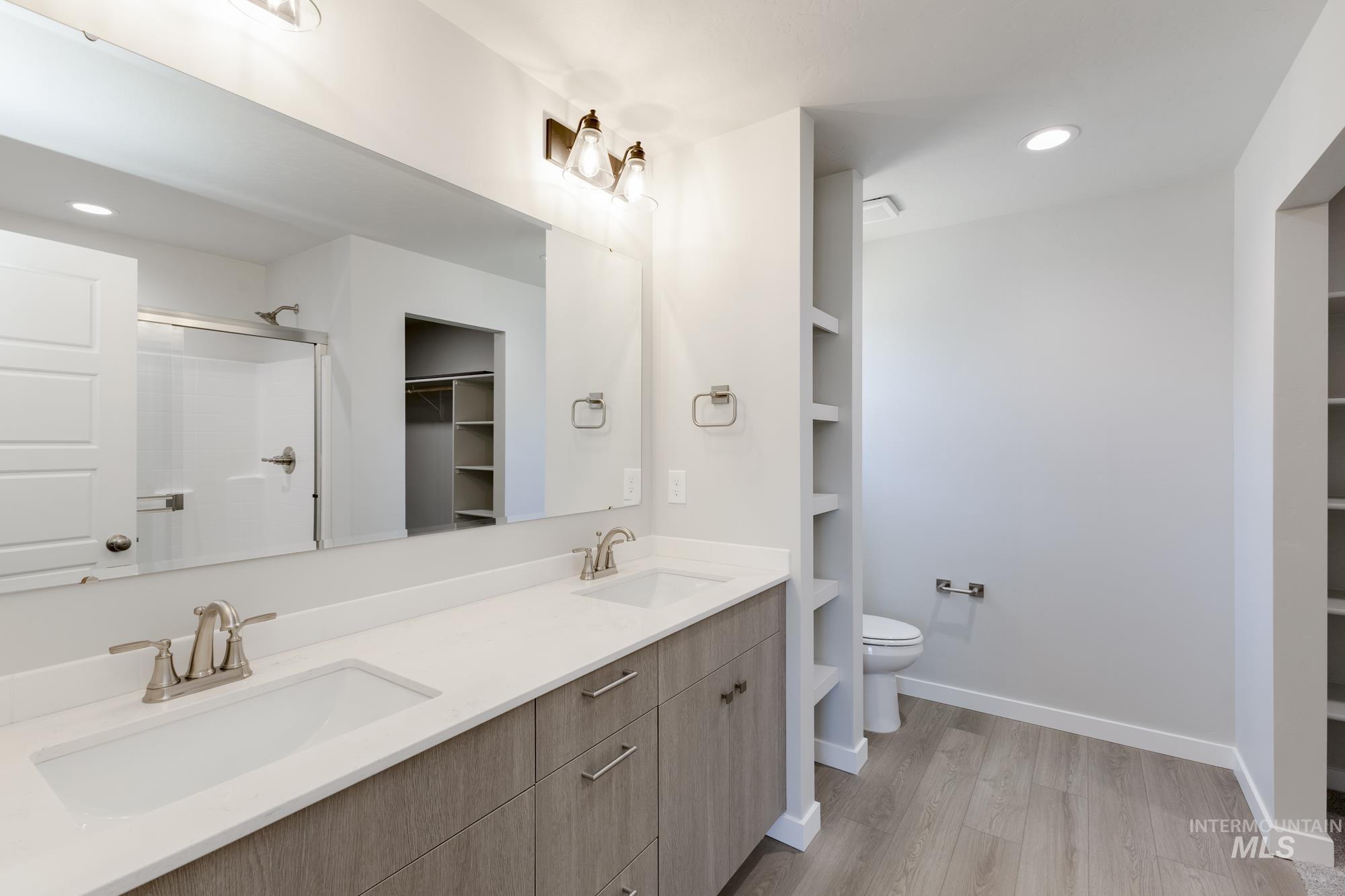 Full bathroom with recessed lighting, a spacious closet, wood finished floors, double vanity, and a shower with door