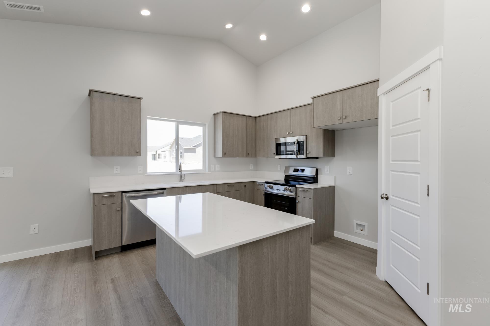 Kitchen with stainless steel appliances, modern cabinets, light wood finished floors, light countertops, and high vaulted ceiling