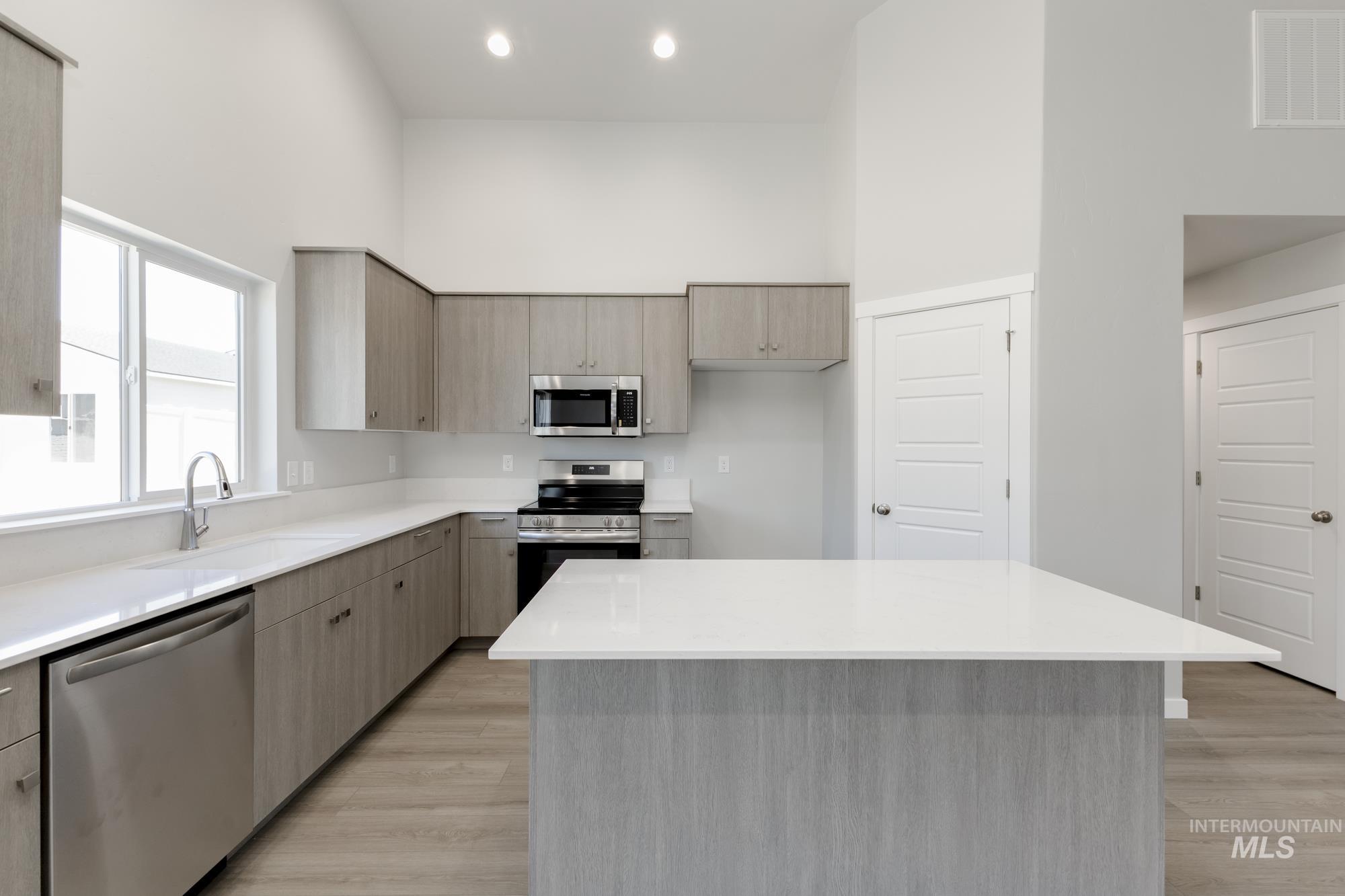 Kitchen featuring appliances with stainless steel finishes, a high ceiling, light wood-style flooring, light countertops, and a center island