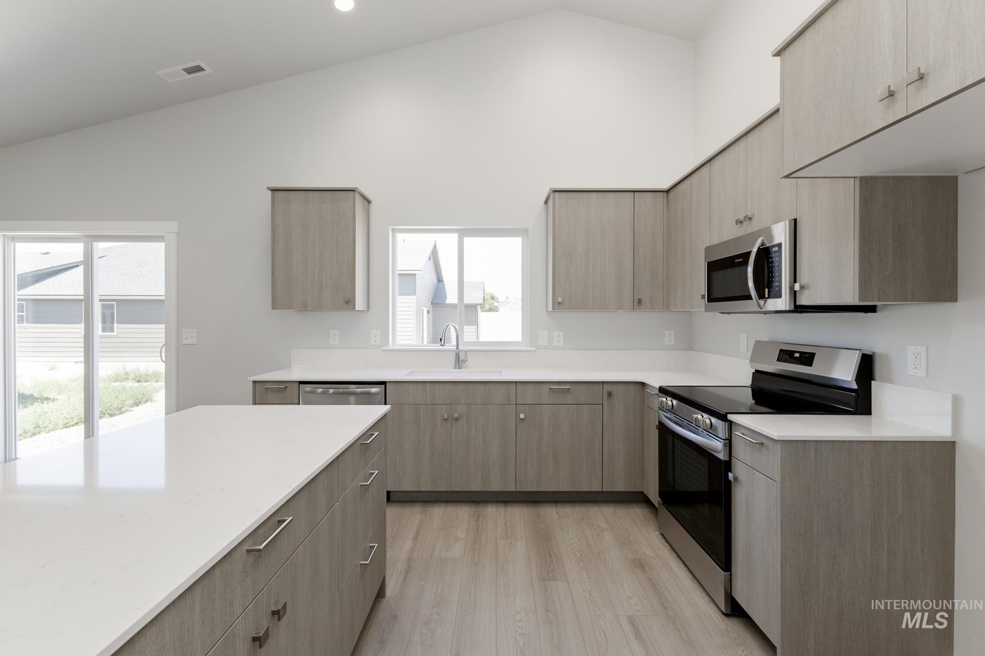 Kitchen featuring stainless steel appliances, light countertops, light wood-style flooring, high vaulted ceiling, and light brown cabinetry