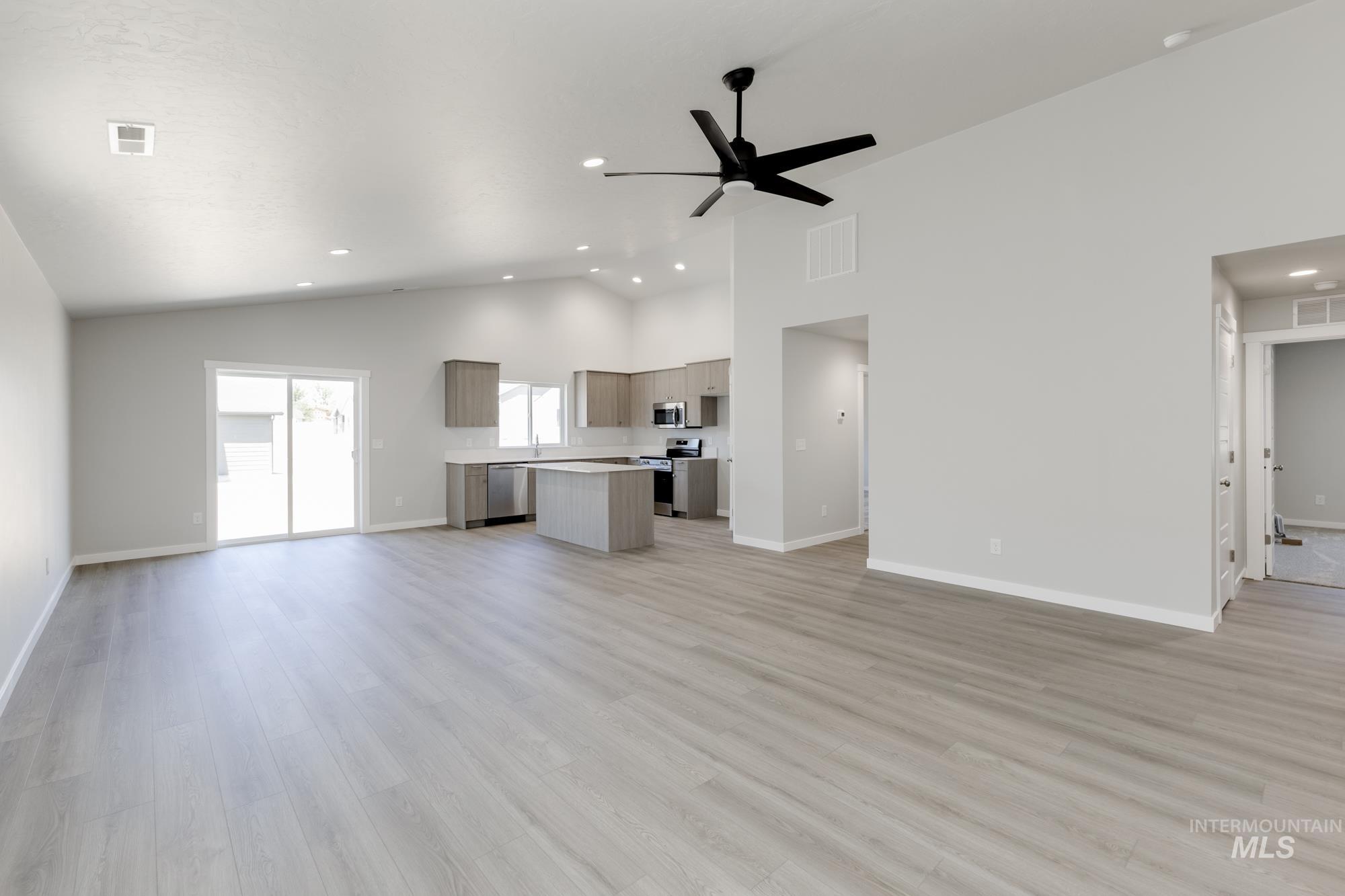 Unfurnished living room with light wood-type flooring, ceiling fan, high vaulted ceiling, and recessed lighting