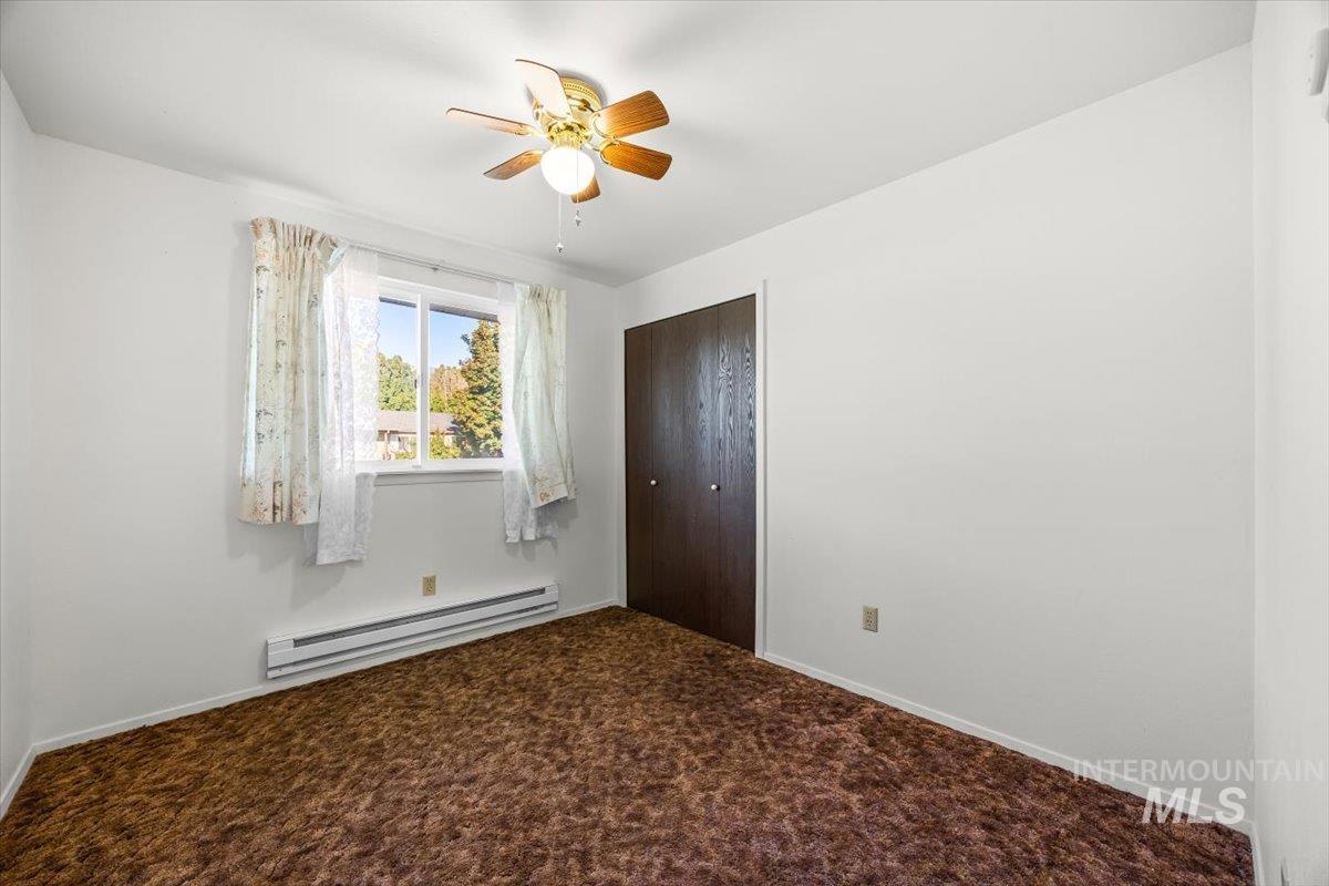 Unfurnished bedroom with a baseboard heating unit, carpet, a closet, and ceiling fan