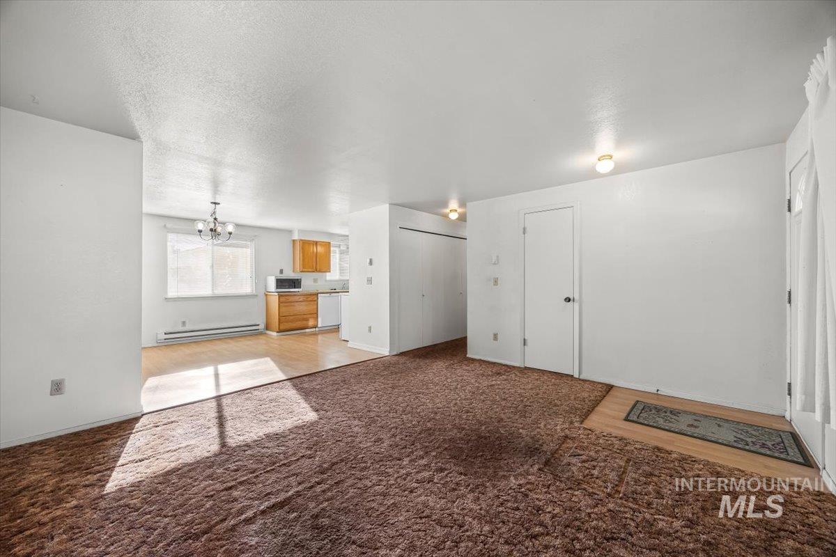 Unfurnished living room with a chandelier, light carpet, a baseboard heating unit, and a textured ceiling