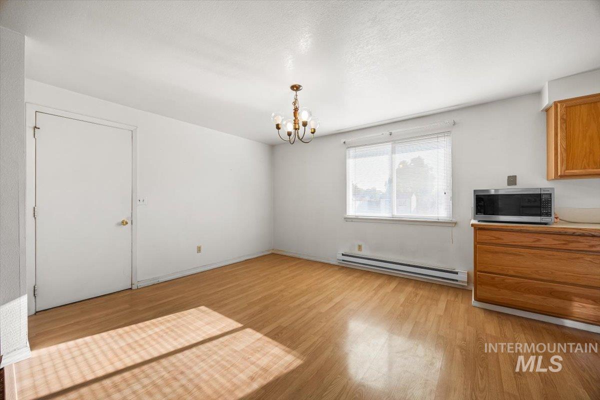 Unfurnished dining area with a baseboard radiator, light wood-style flooring, a chandelier, and a textured ceiling