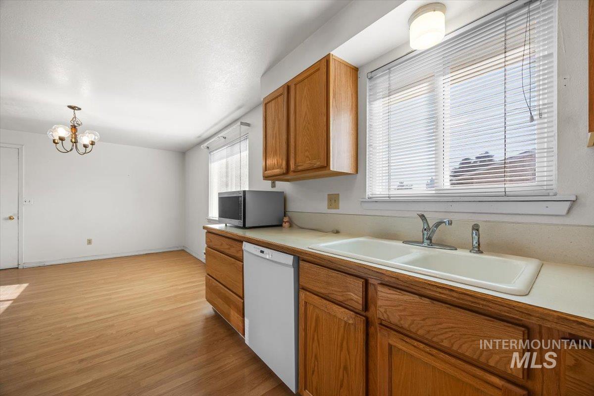 Kitchen featuring dishwasher, light countertops, a chandelier, stainless steel microwave, and brown cabinetry