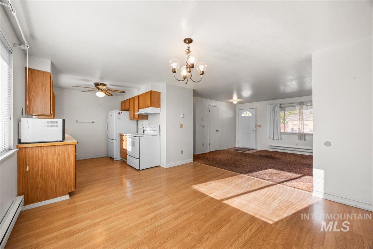 Kitchen featuring brown cabinets, a baseboard heating unit, white appliances, light countertops, and light wood-style flooring