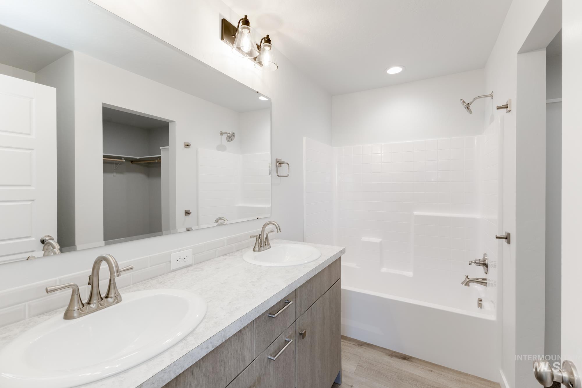 Full bathroom with shower / bath combination, light wood-style floors, double vanity, a spacious closet, and recessed lighting