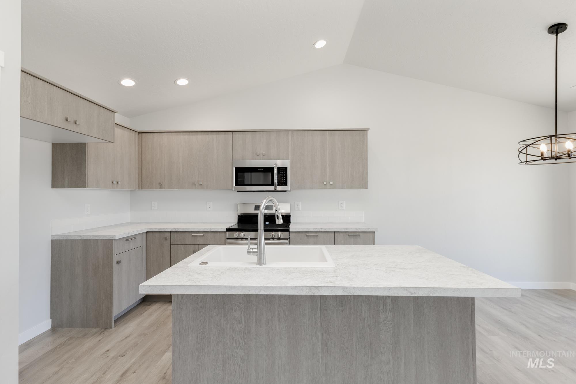 Kitchen with light brown cabinets, modern cabinets, appliances with stainless steel finishes, an island with sink, and lofted ceiling