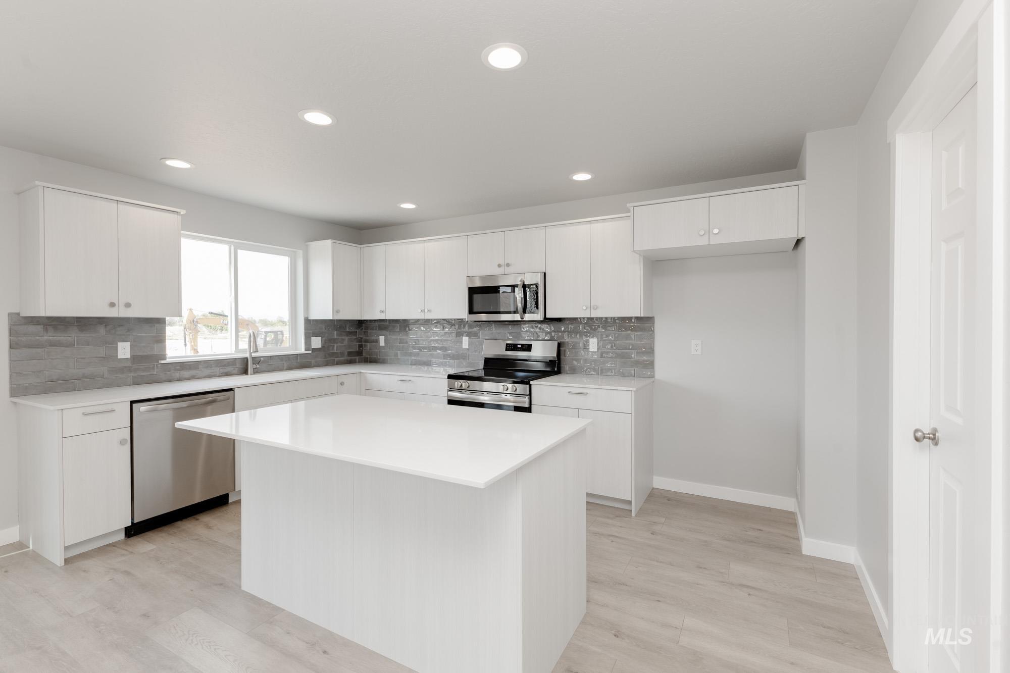 Kitchen with stainless steel appliances, decorative backsplash, white cabinetry, recessed lighting, and a center island