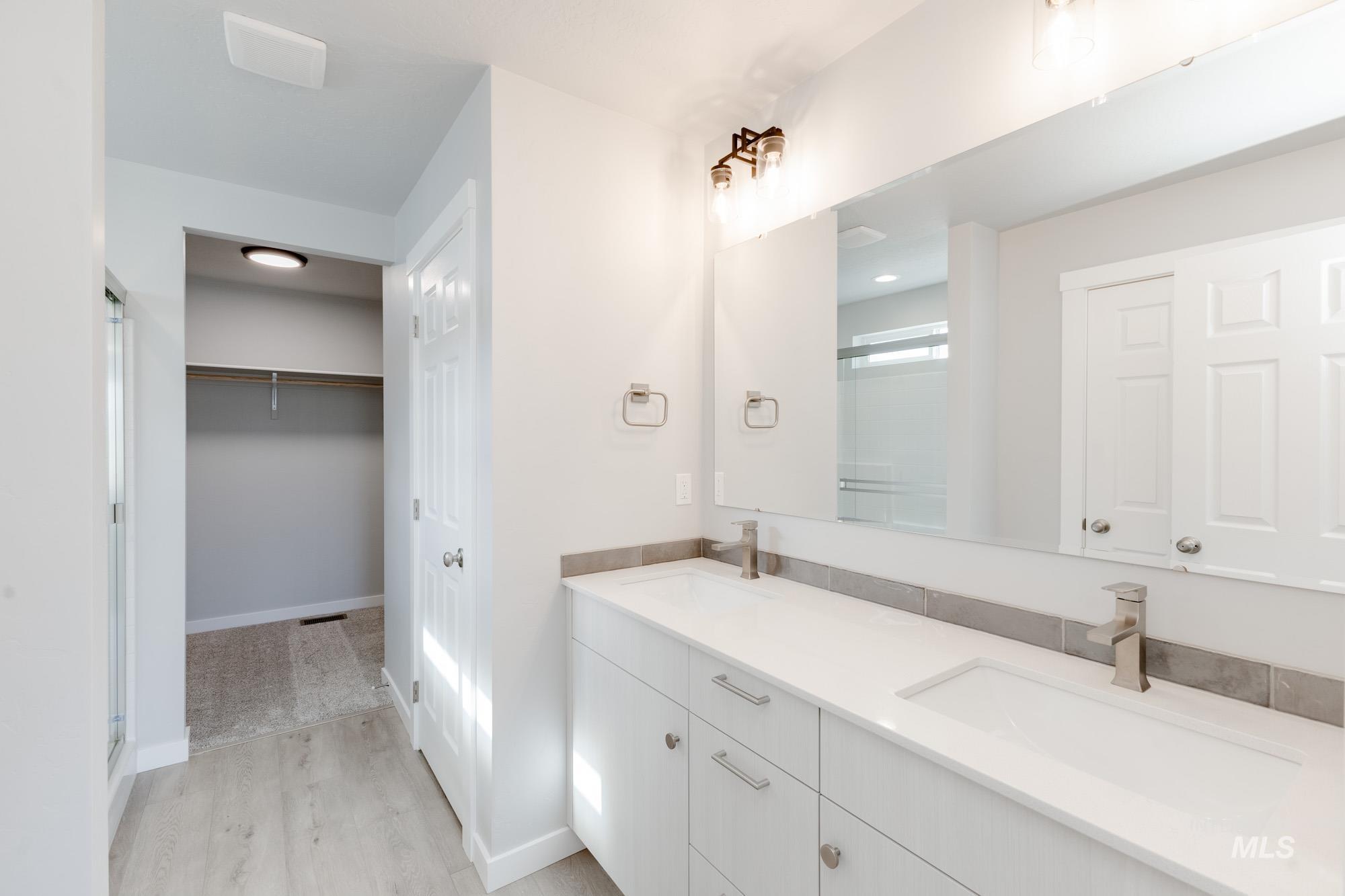 Bathroom featuring wood finished floors, a stall shower, double vanity, and a spacious closet