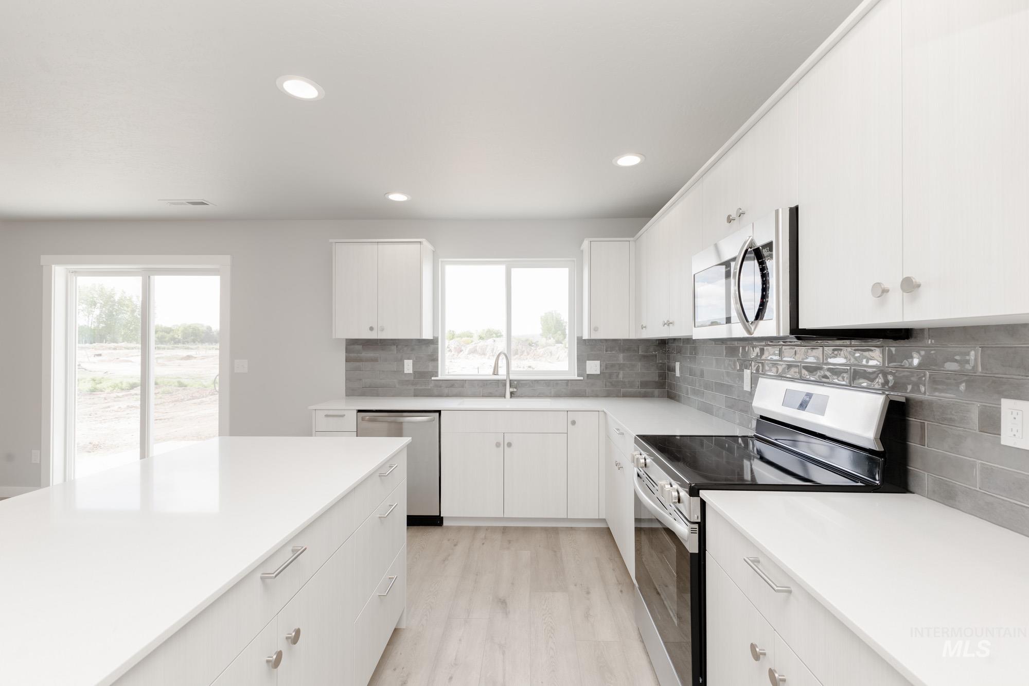 Kitchen with stainless steel appliances, light wood-style flooring, backsplash, recessed lighting, and light countertops