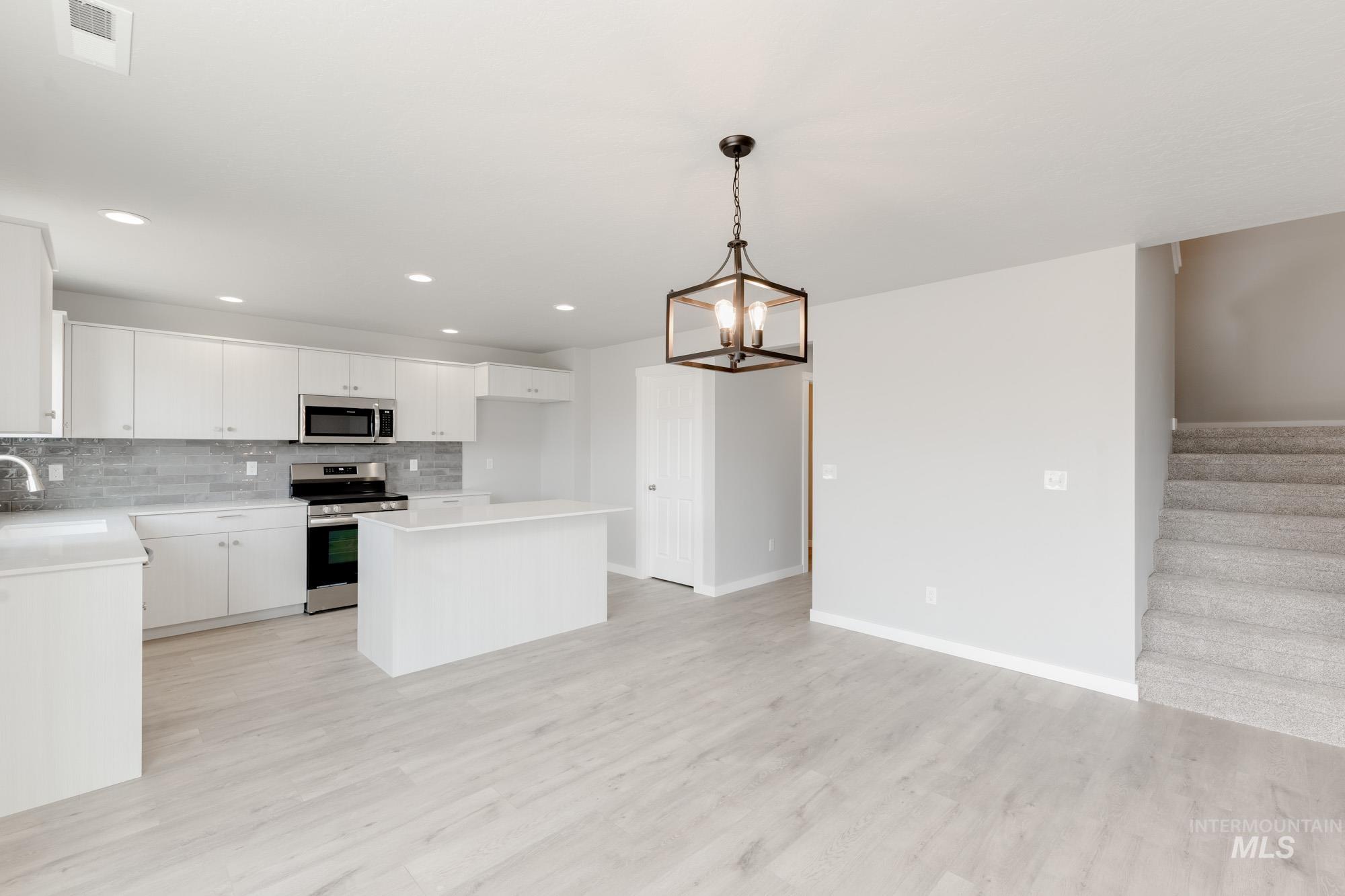 Kitchen featuring appliances with stainless steel finishes, a kitchen island, open floor plan, white cabinets, and backsplash