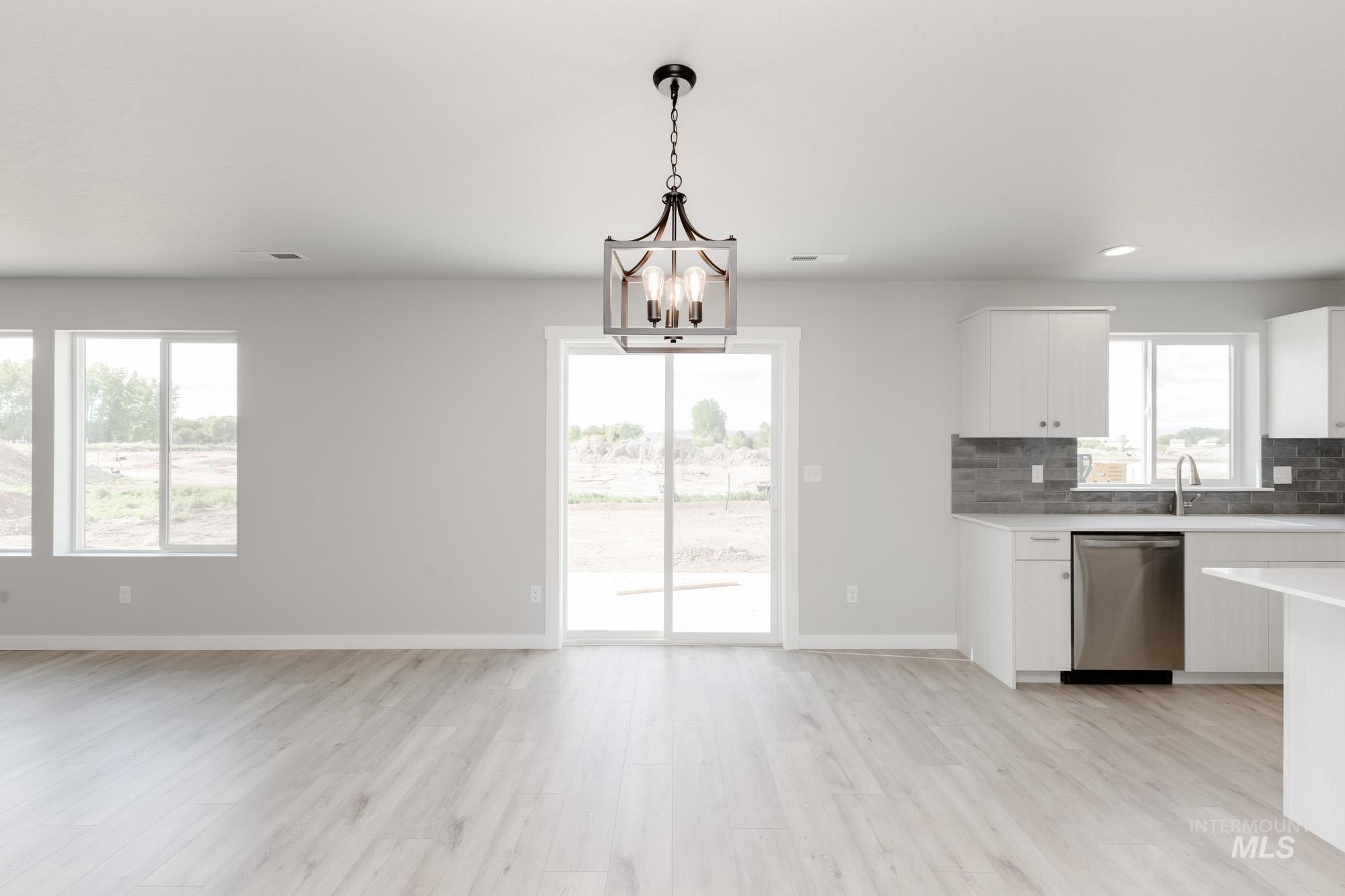 Kitchen featuring stainless steel dishwasher, white cabinets, a chandelier, tasteful backsplash, and light wood finished floors