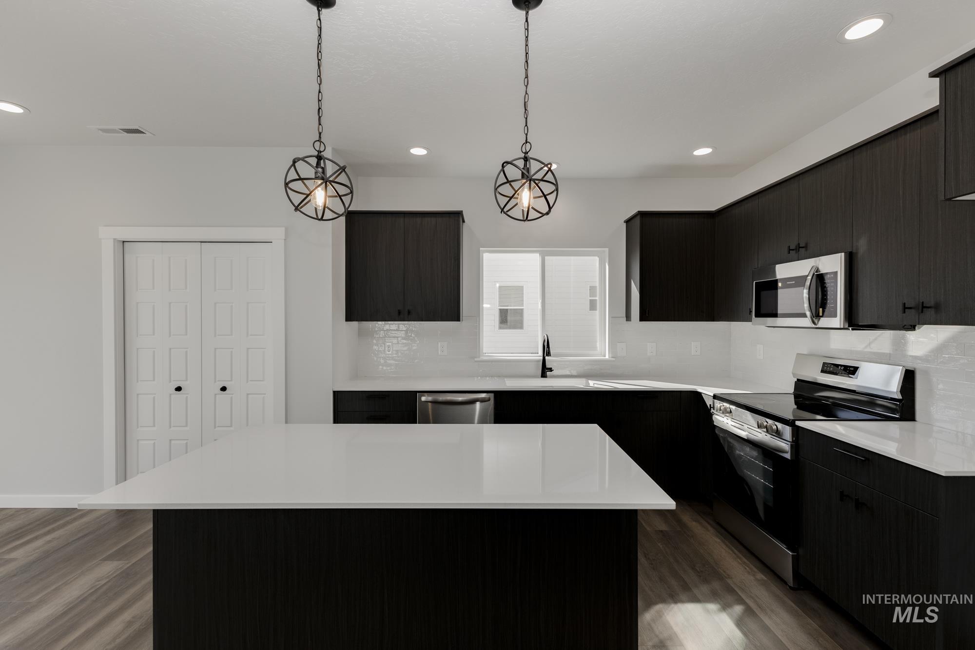 Kitchen featuring appliances with stainless steel finishes, a center island, hanging light fixtures, dark wood-style floors, and dark cabinets