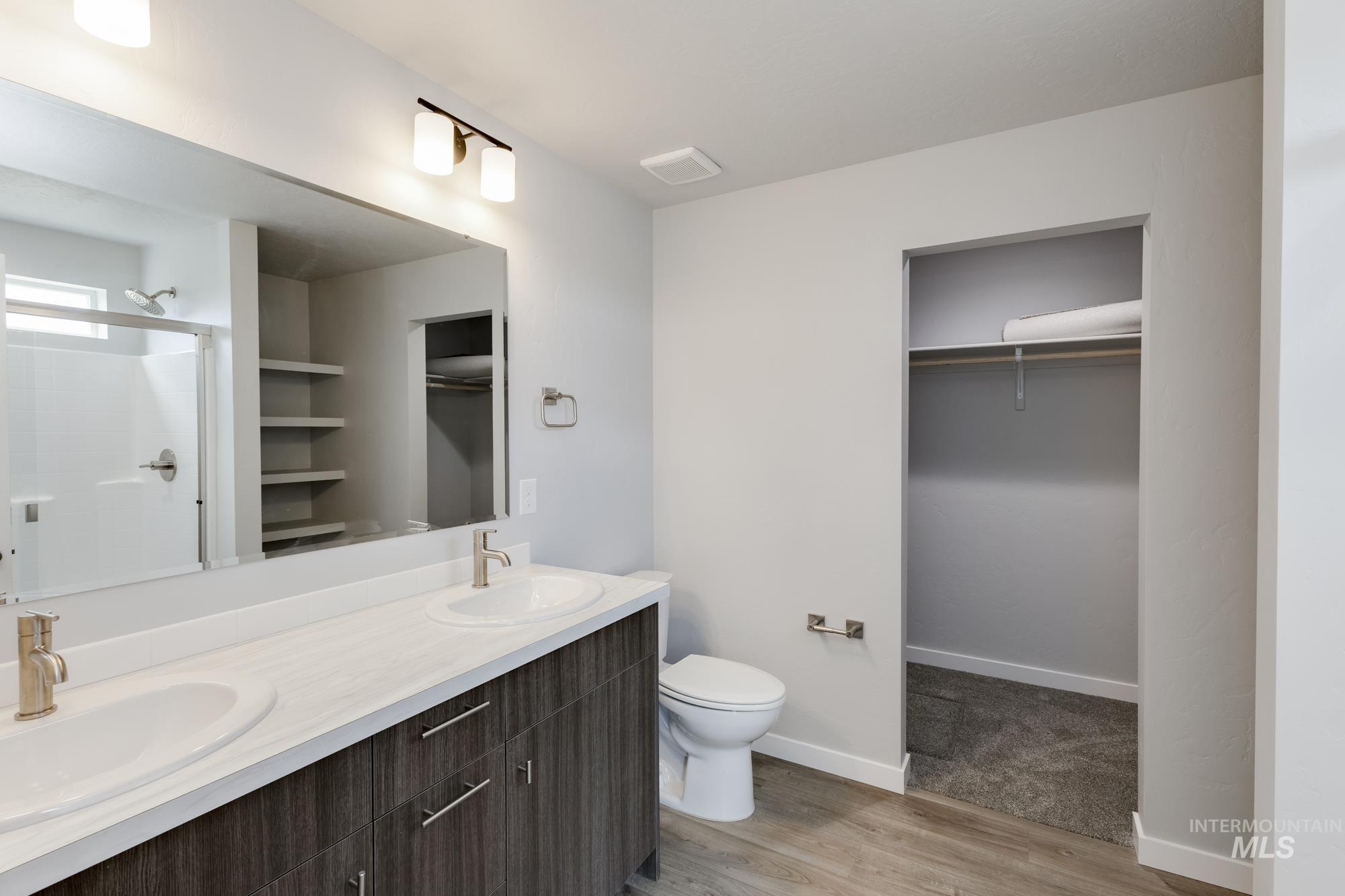 Bathroom with a spacious closet, light wood-style floors, double vanity, and a shower