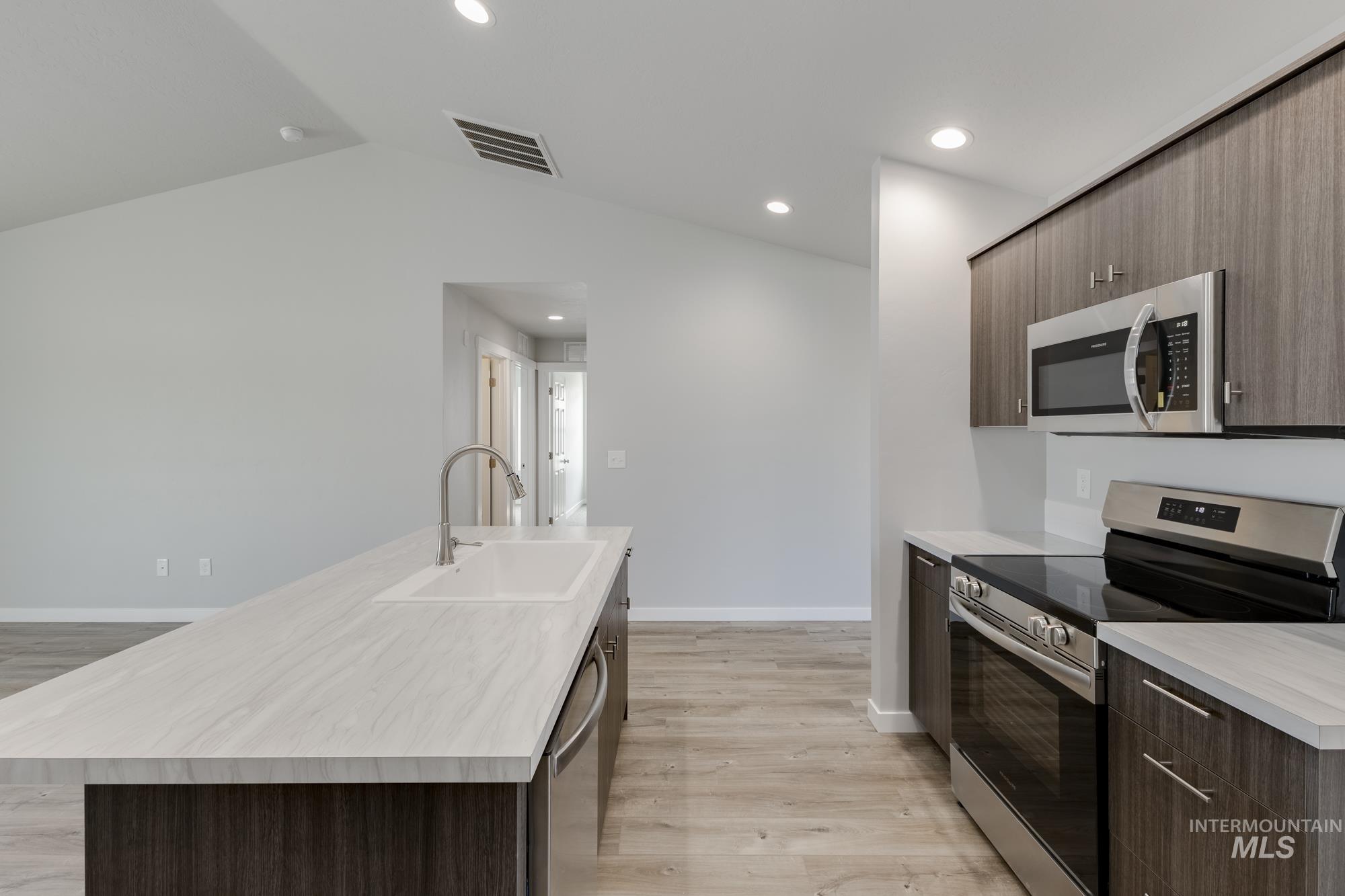 Kitchen featuring appliances with stainless steel finishes, dark brown cabinets, light countertops, modern cabinets, and light wood-style flooring