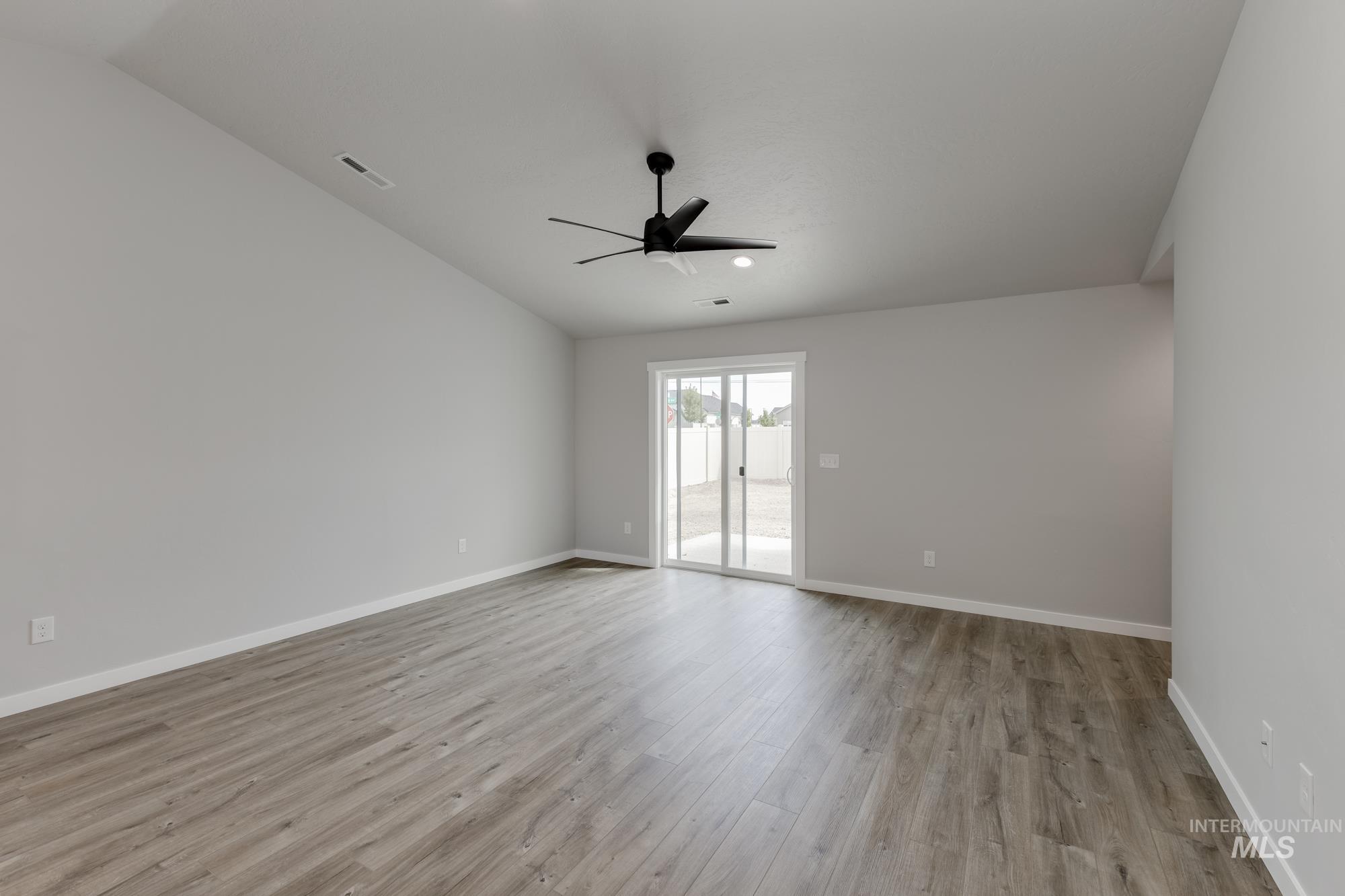 Empty room featuring light wood finished floors, vaulted ceiling, and a ceiling fan