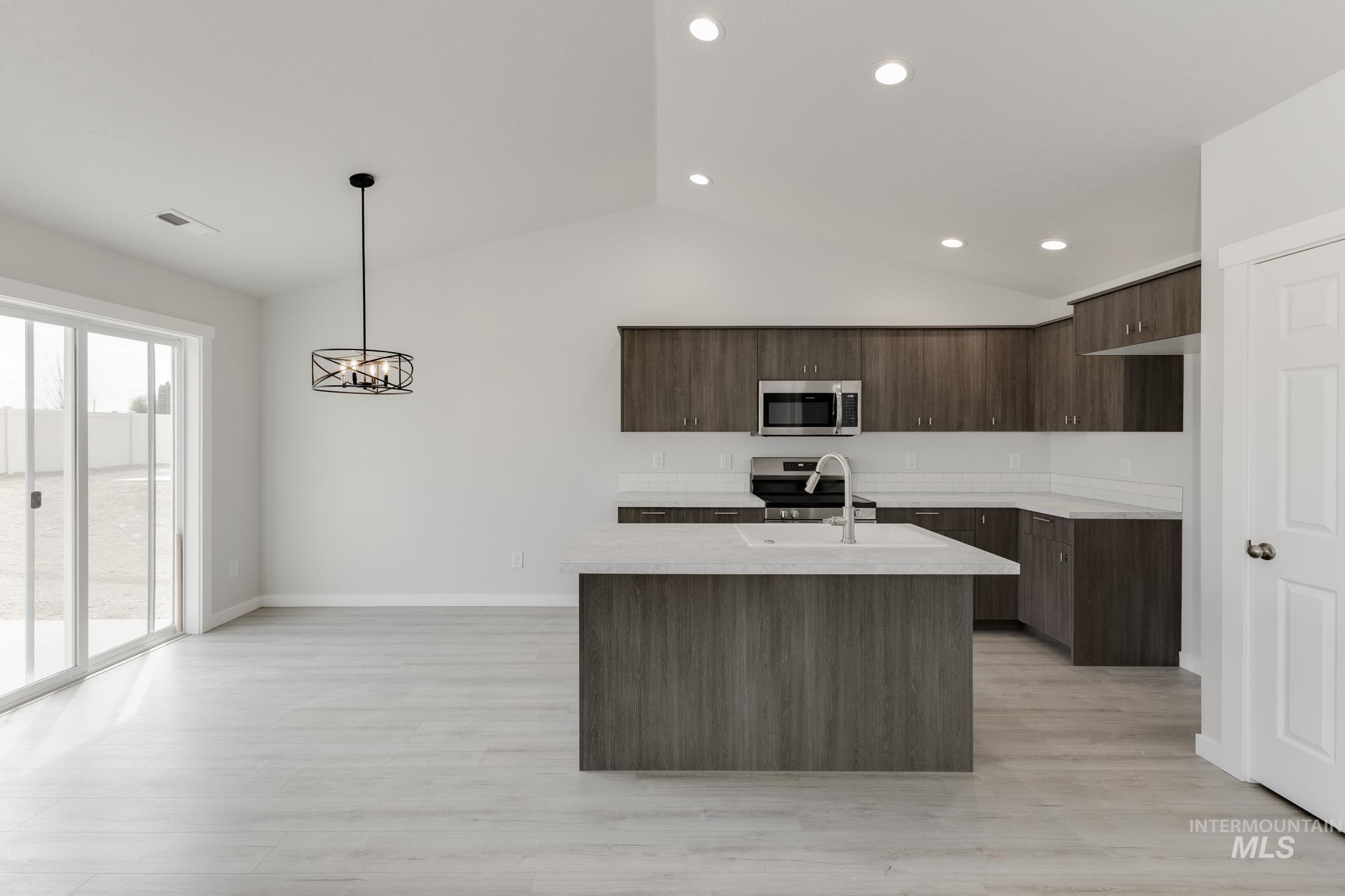 Kitchen with dark brown cabinets, vaulted ceiling, an island with sink, stainless steel appliances, and modern cabinets