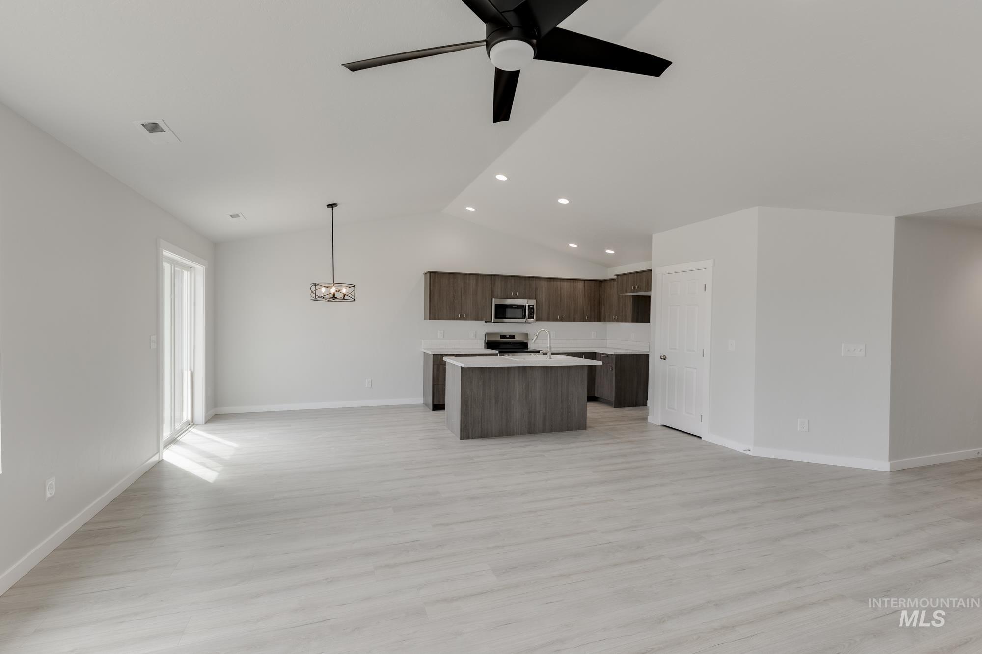 Kitchen featuring open floor plan, light countertops, lofted ceiling, light wood-type flooring, and an island with sink