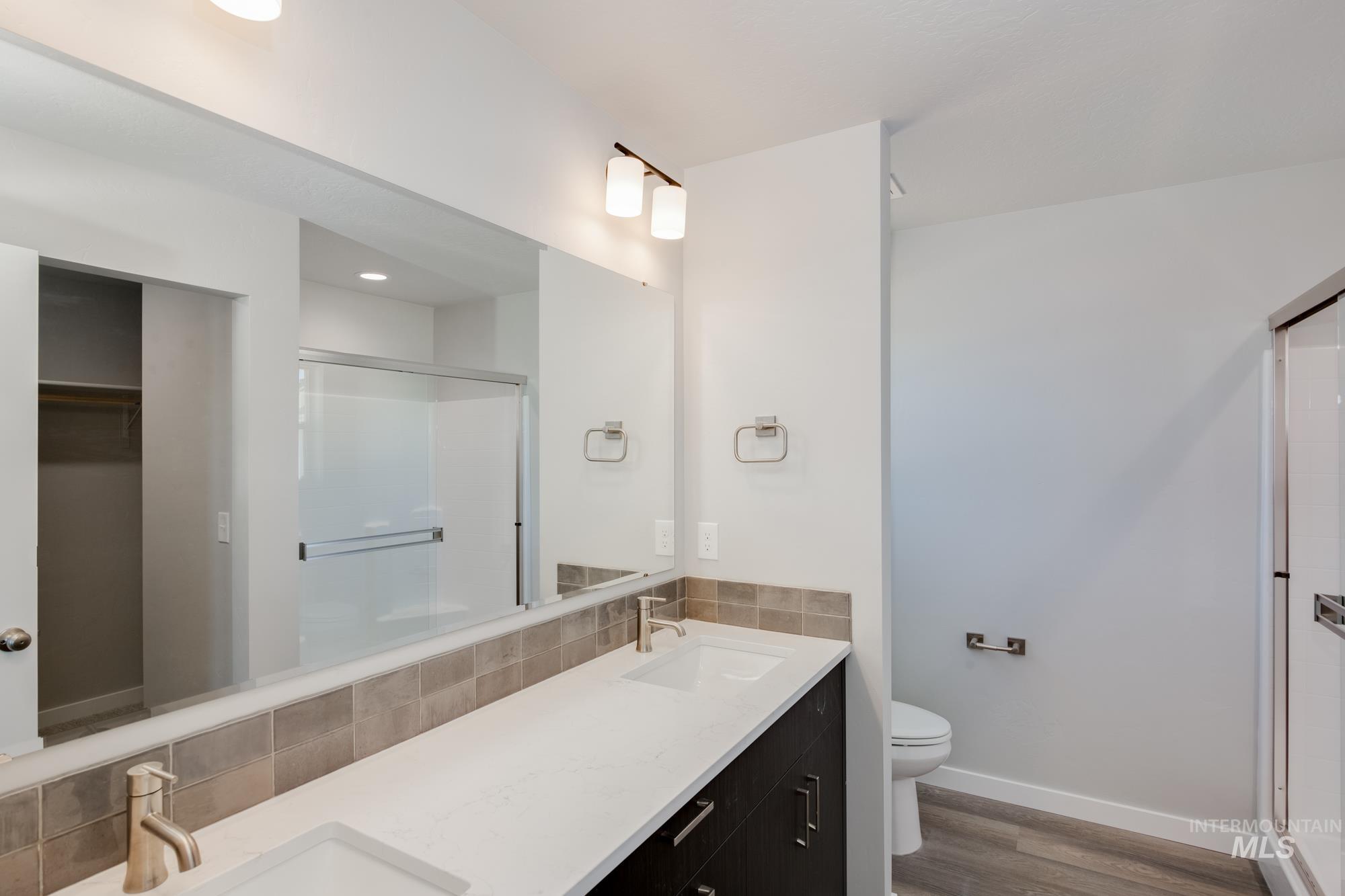 Bathroom with a shower stall, double vanity, wood finished floors, backsplash, and a walk in closet