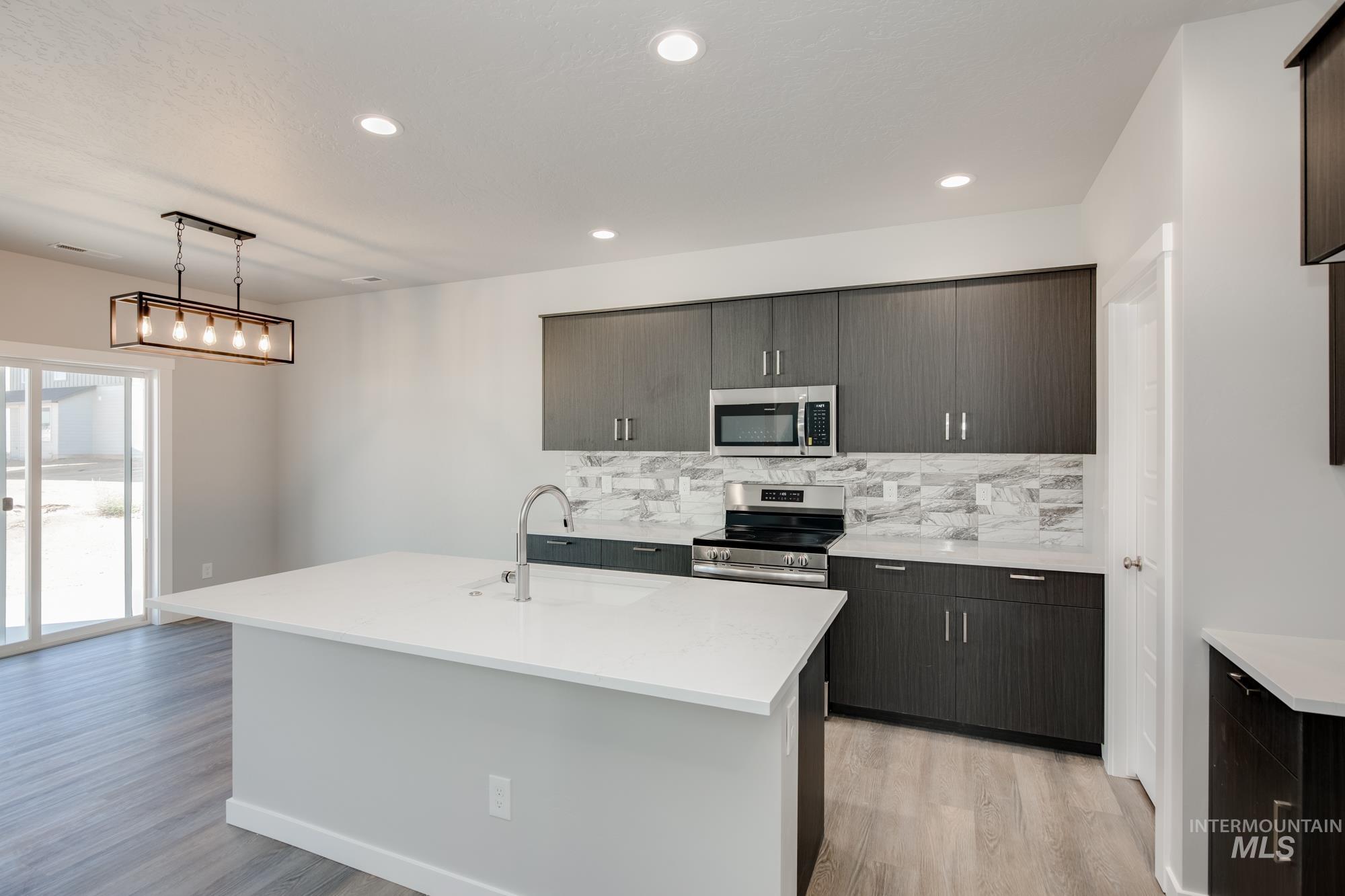 Kitchen with stainless steel appliances, light countertops, light wood-type flooring, backsplash, and recessed lighting