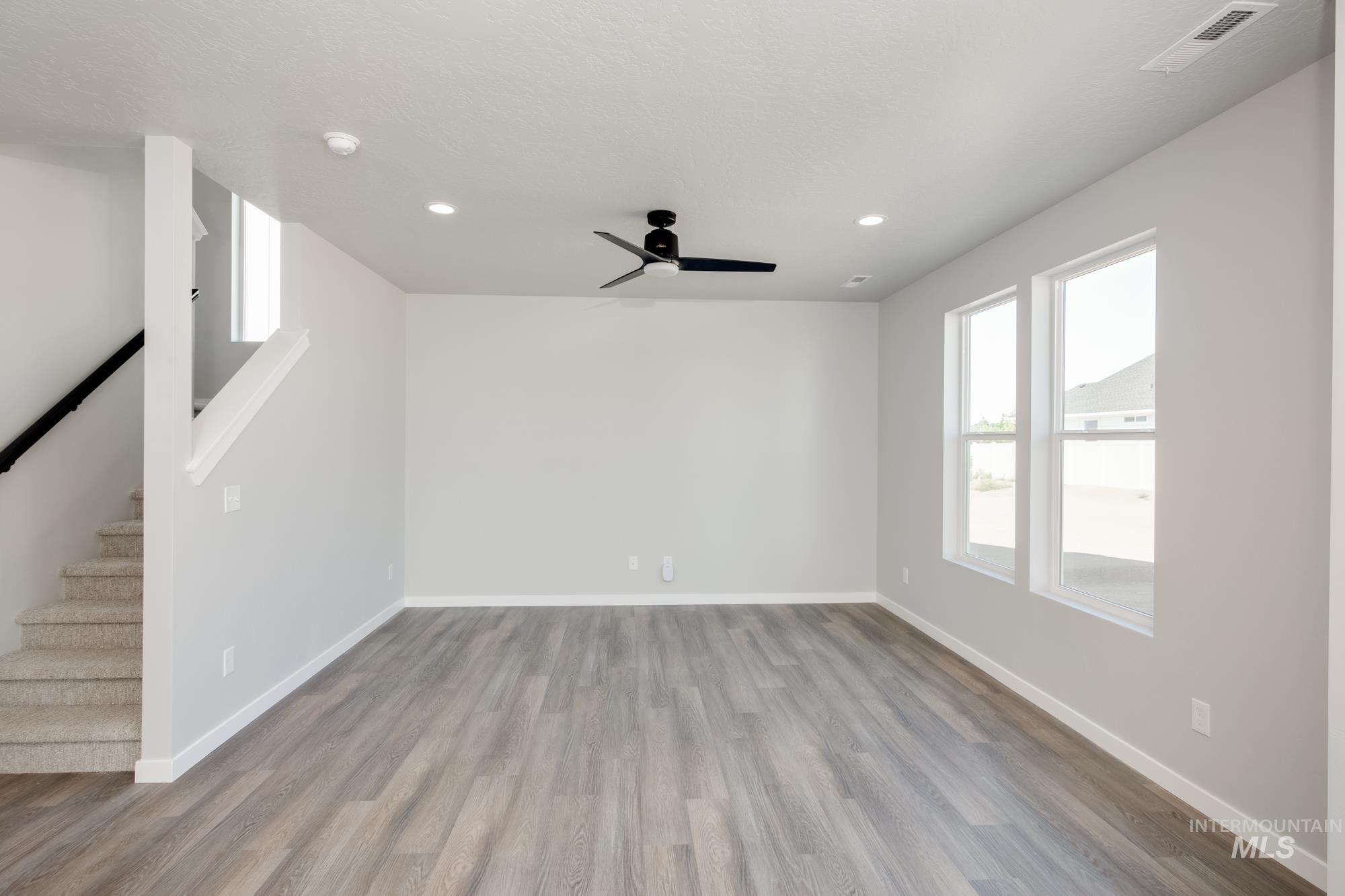 Unfurnished living room with healthy amount of natural light, wood finished floors, stairs, ceiling fan, and recessed lighting