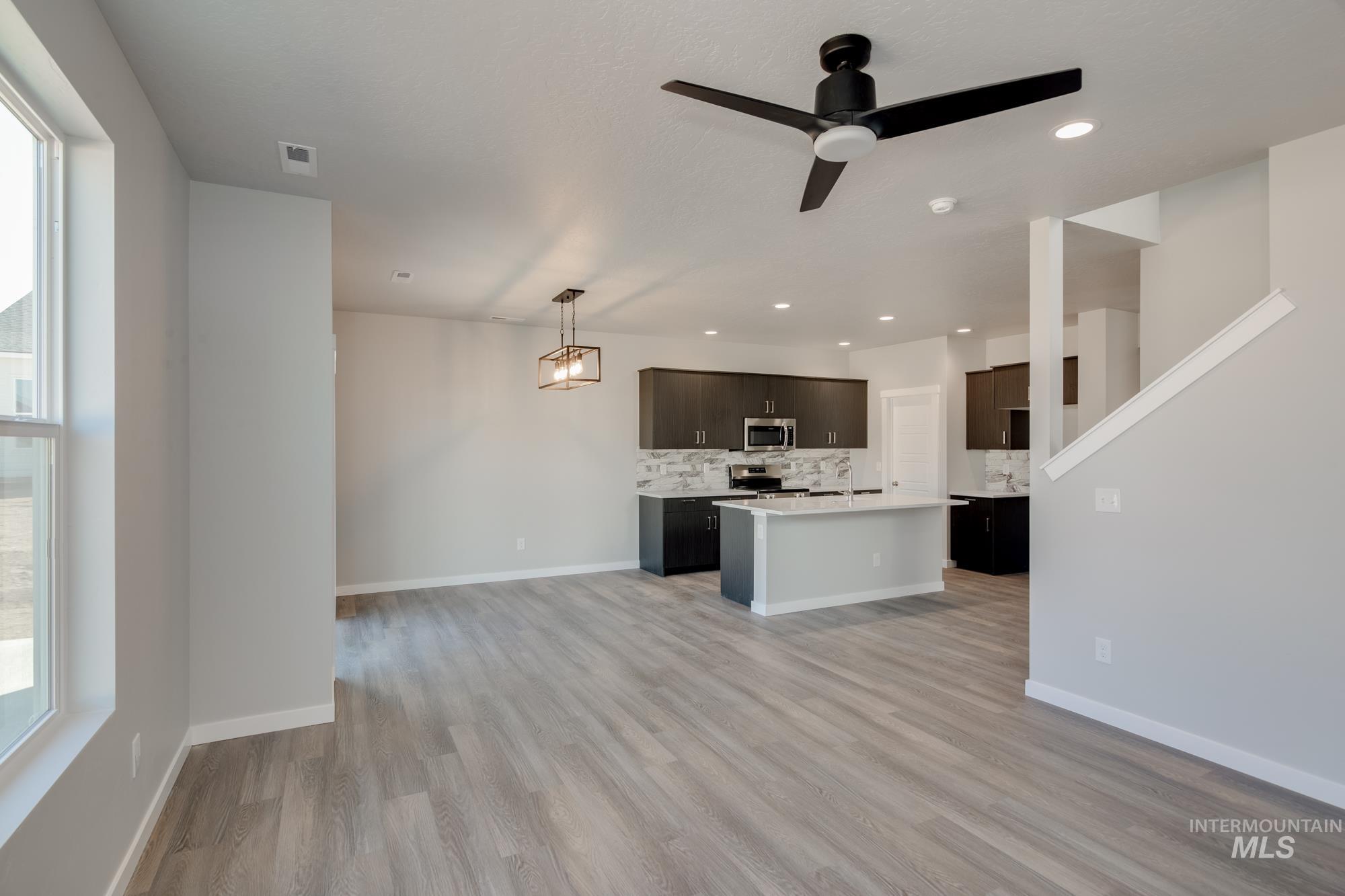 Kitchen with light countertops, decorative backsplash, light wood-style flooring, open floor plan, and a kitchen island with sink