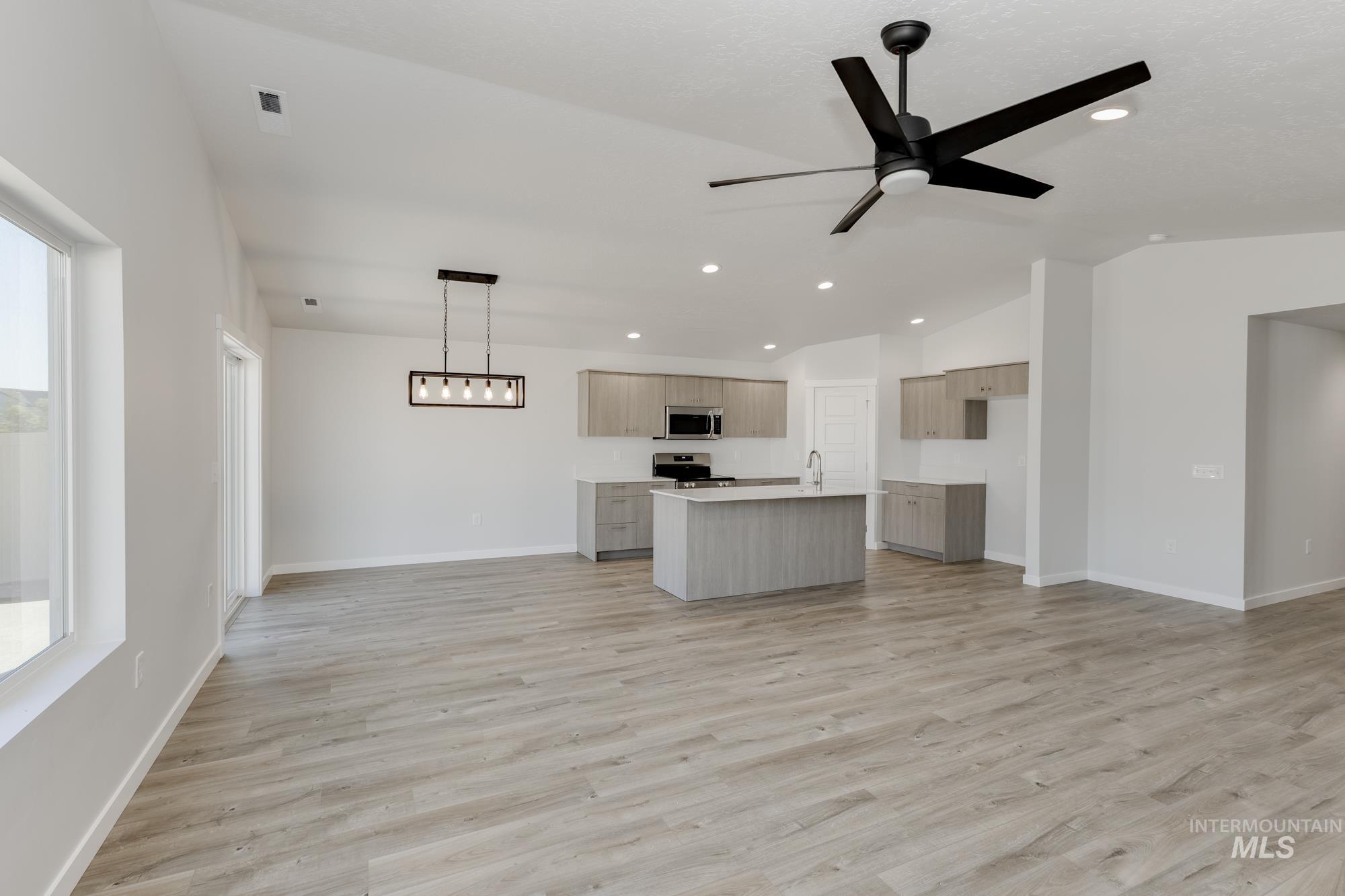 Kitchen featuring open floor plan, lofted ceiling, light countertops, light wood-style flooring, and a kitchen island with sink