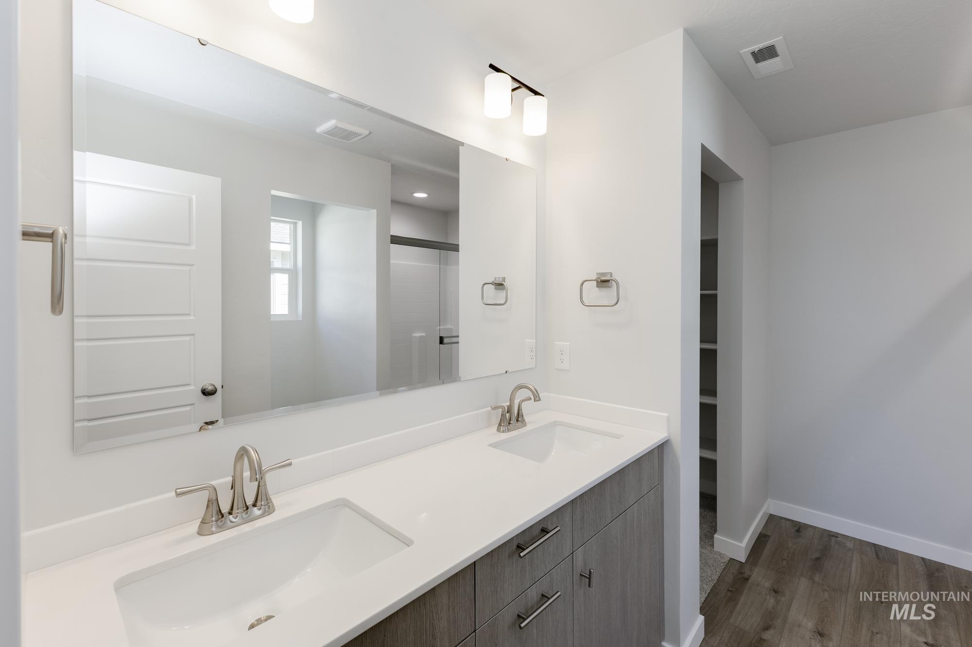 Bathroom with double vanity, dark wood-style flooring, a shower with shower door, and a spacious closet