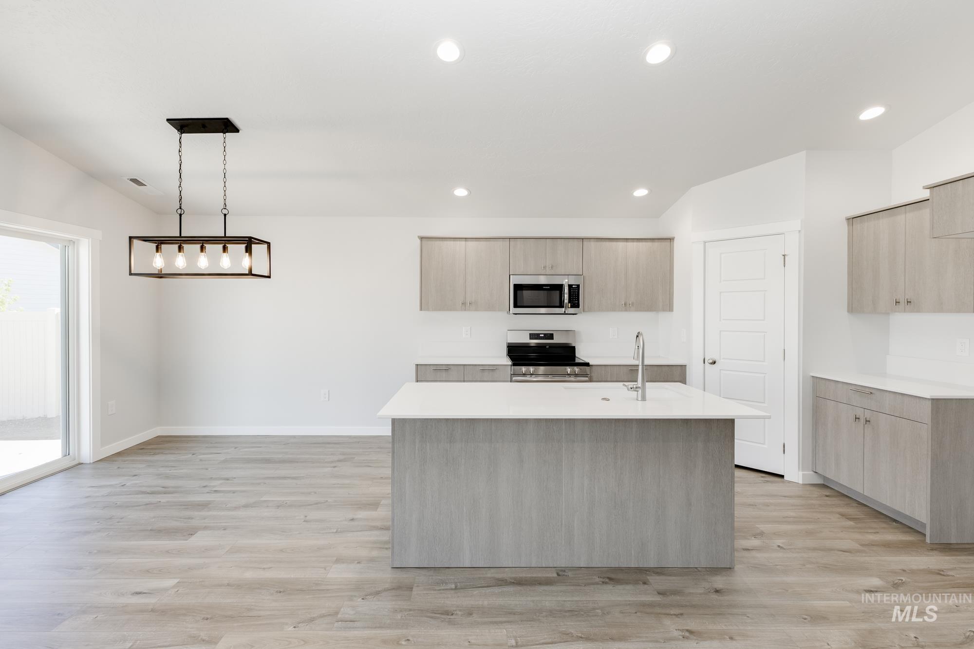 Kitchen featuring an island with sink, stainless steel appliances, light wood-style flooring, decorative light fixtures, and light stone counters